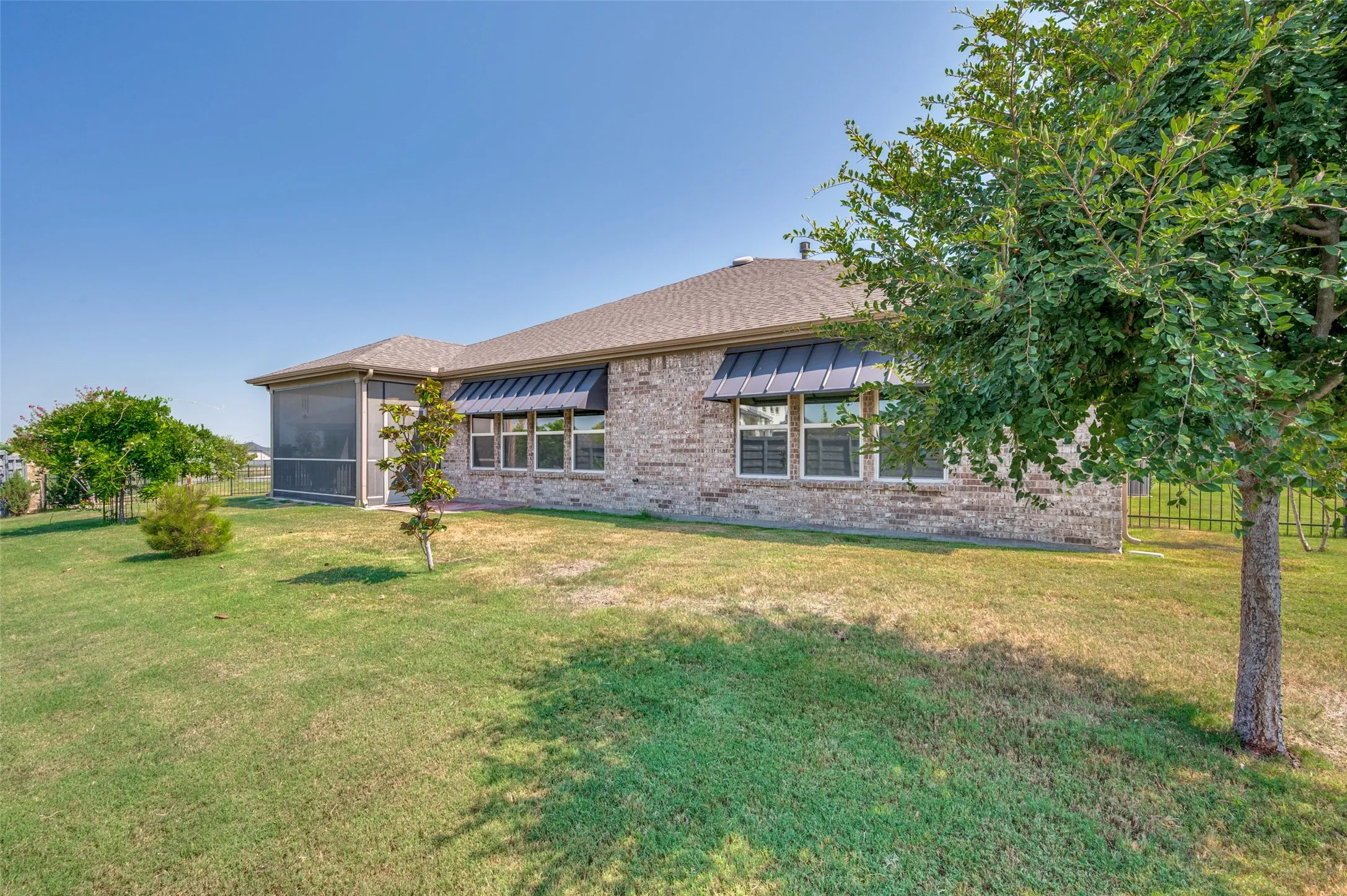 Expansive backyard featuring a screened patio, a brick exterior, multiple windows with awnings, and mature trees