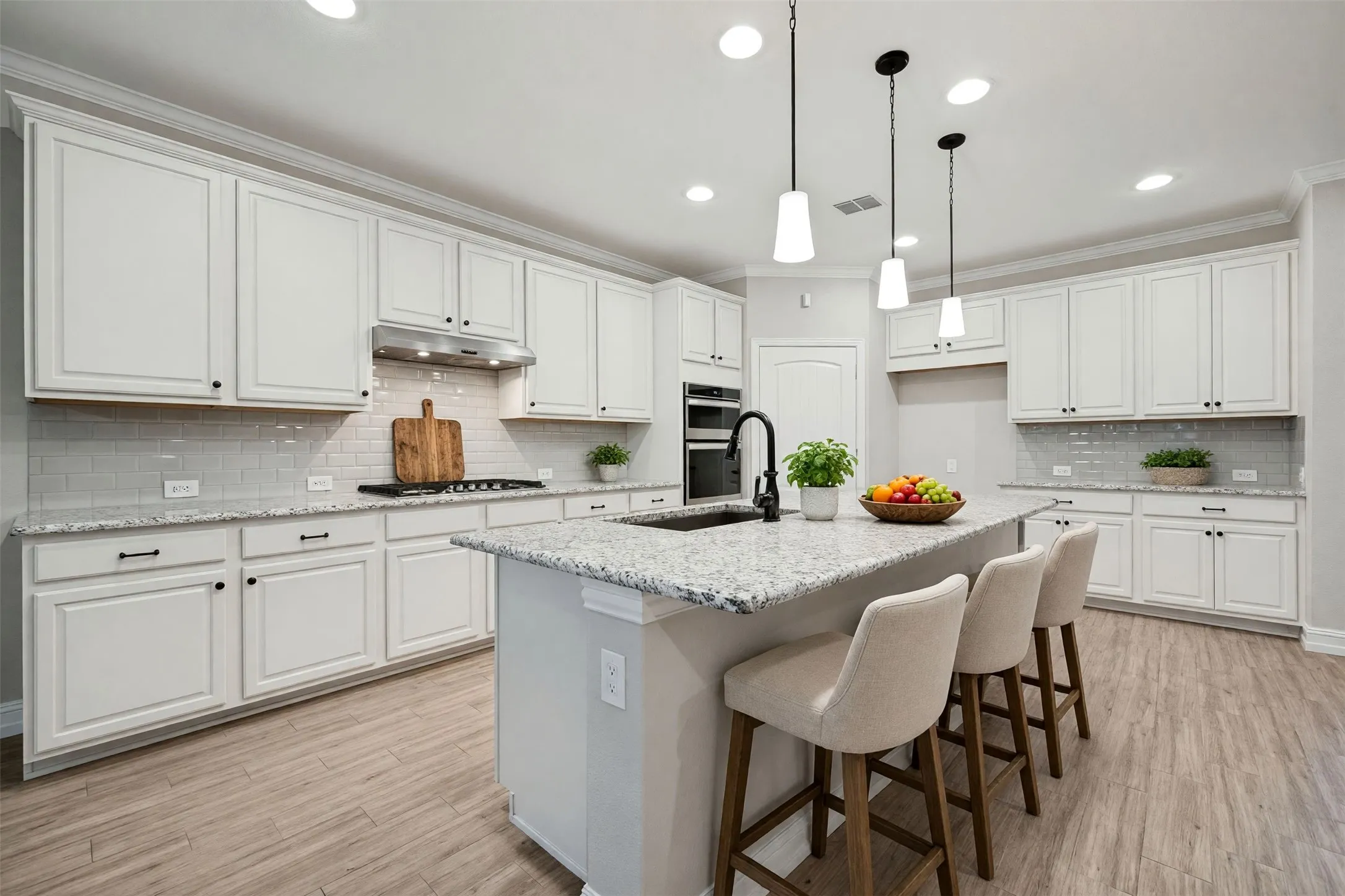 Kitchen featuring white cabinetry, light-colored countertops, a tile backsplash, wood-finish flooring, and pendant lighting/Virtually staged