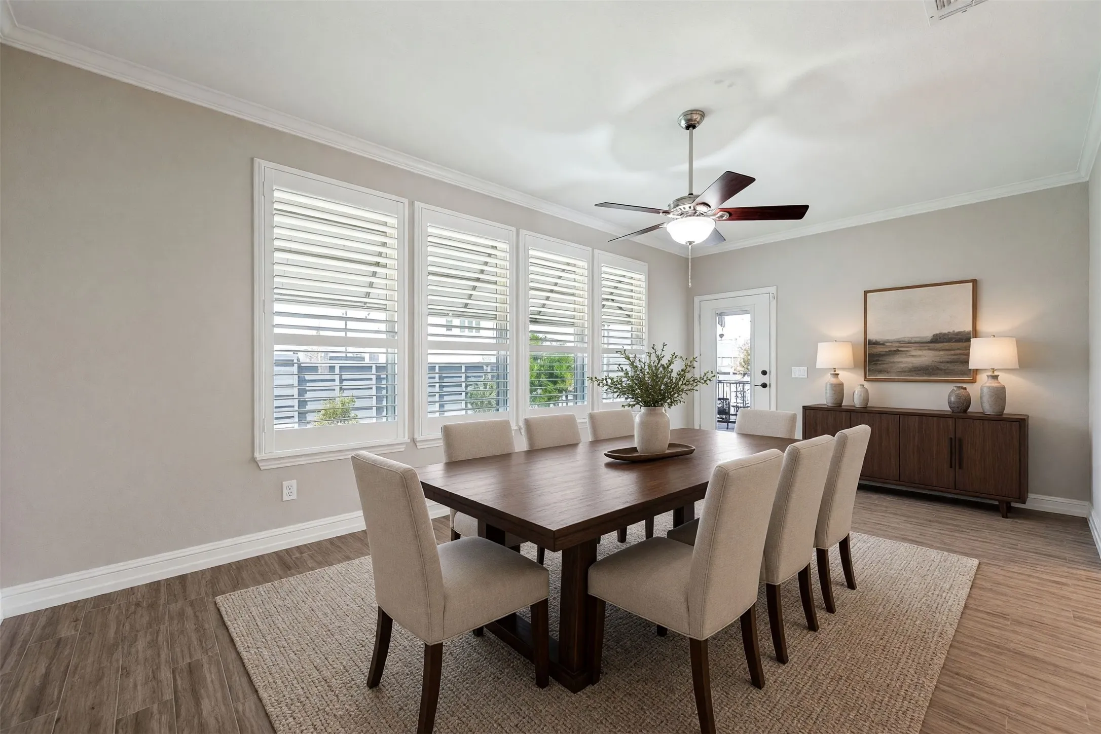 Hardwood-style flooring, white crown molding, multiple windows with plantation shutters, and a ceiling fan with light fixture/ Virtually staged