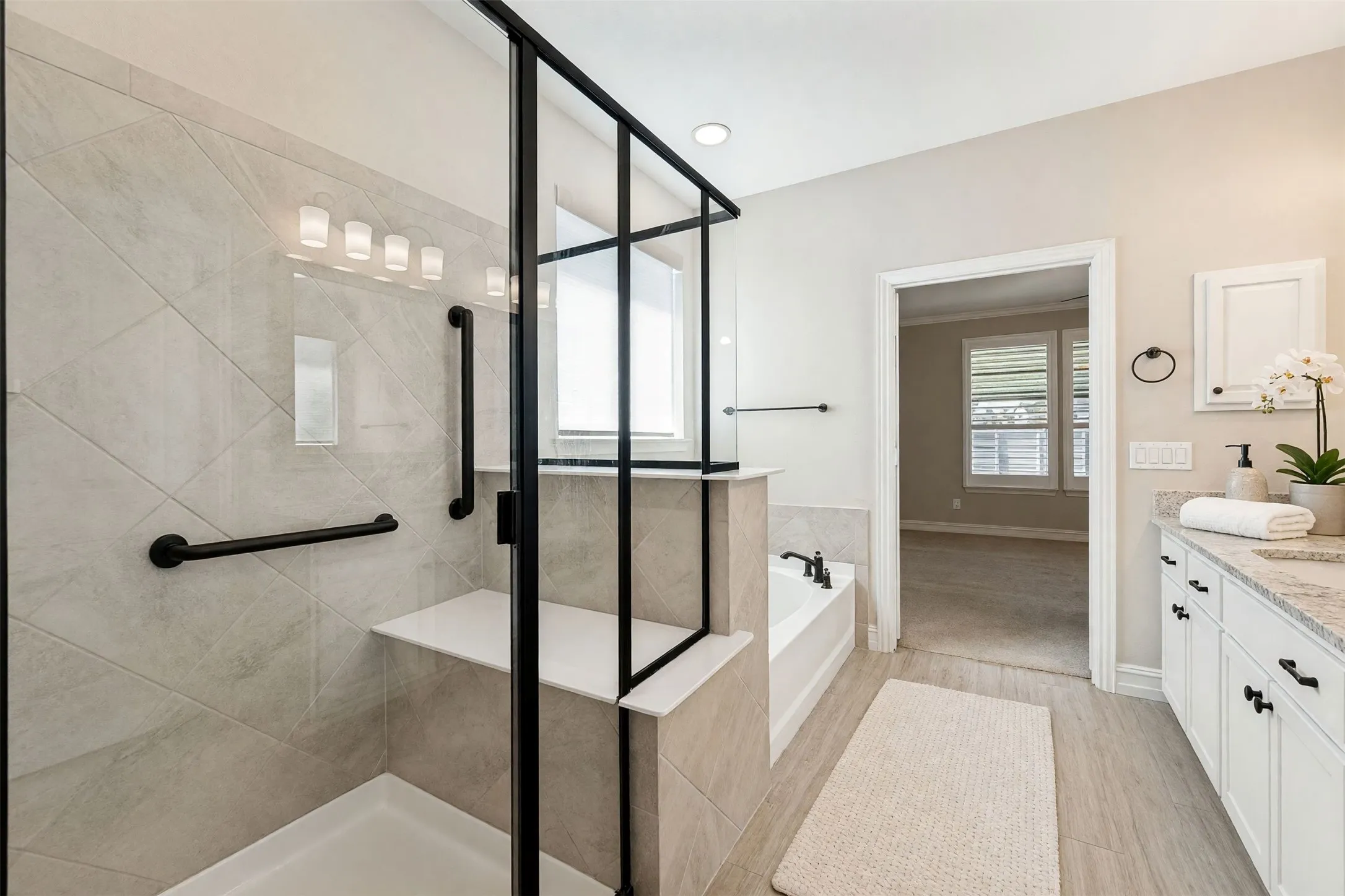 Spacious bathroom featuring a glass-enclosed shower with tiled walls and a built-in bench, a separate soaking tub, and a double vanity with stone countertops and white cabinetry