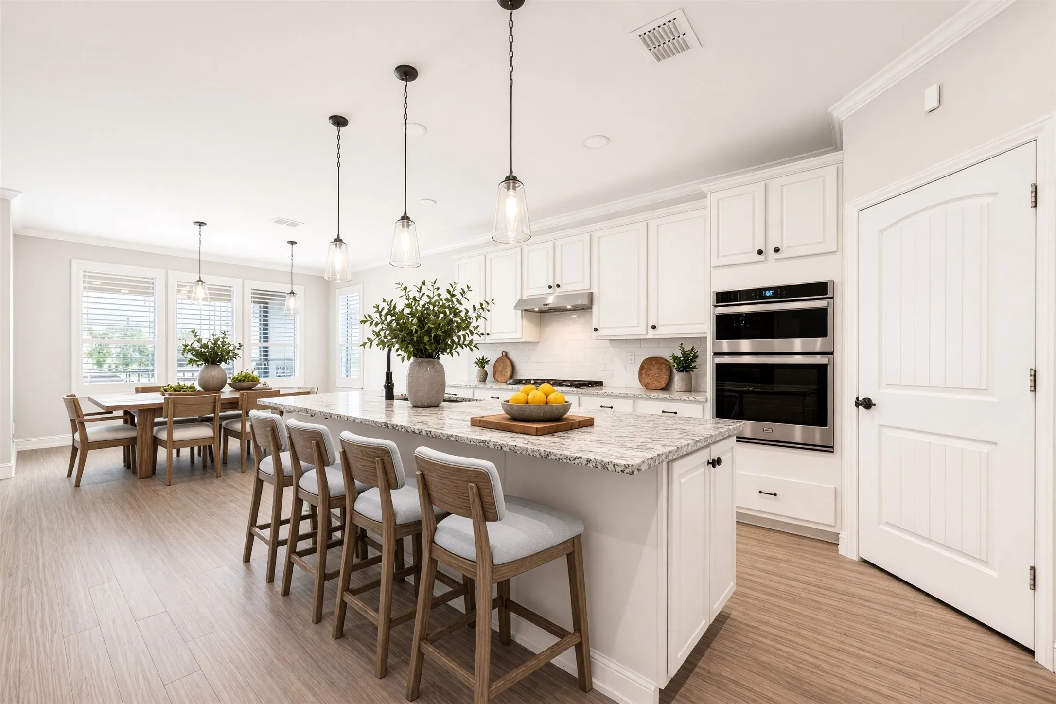 Kitchen featuring a large island with stone countertop, white cabinetry with dark hardware, stainless steel double ovens, and wood-finish flooring/virtually staged