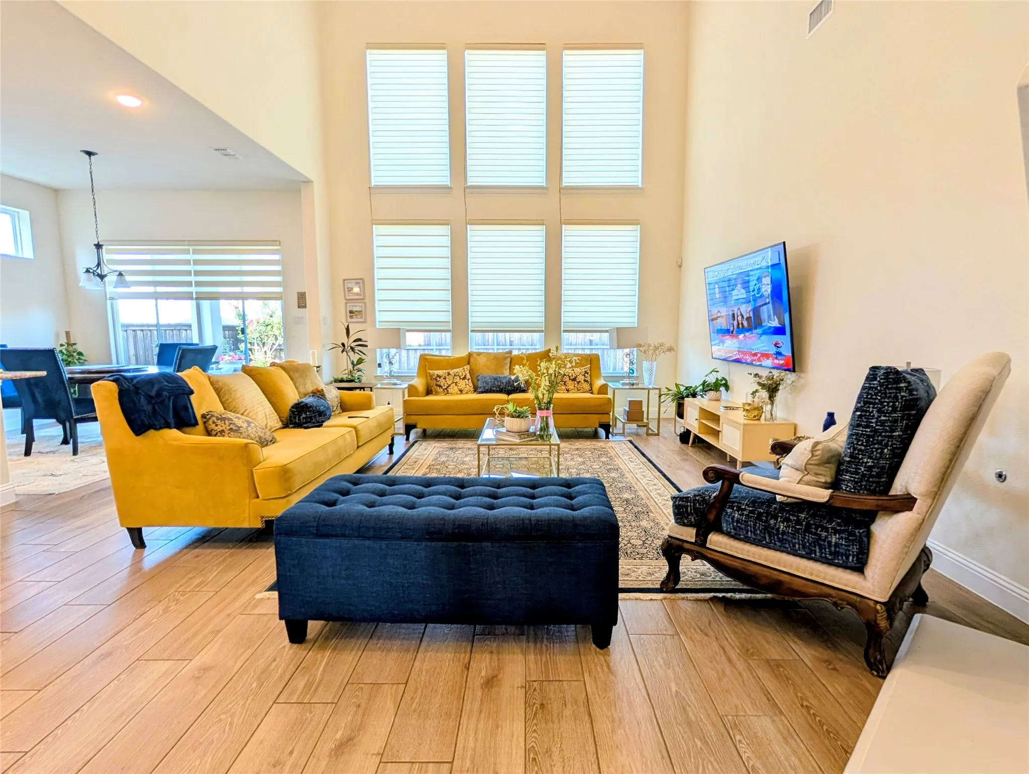 Two-story living area with high ceilings, multiple large windows, wood-finish flooring, and a dining area beyond