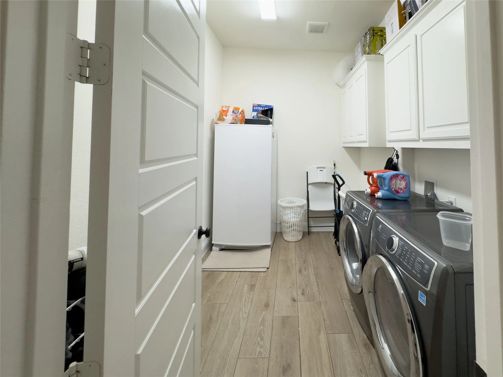 Utility room with wood-finish flooring and white shaker-style cabinetry