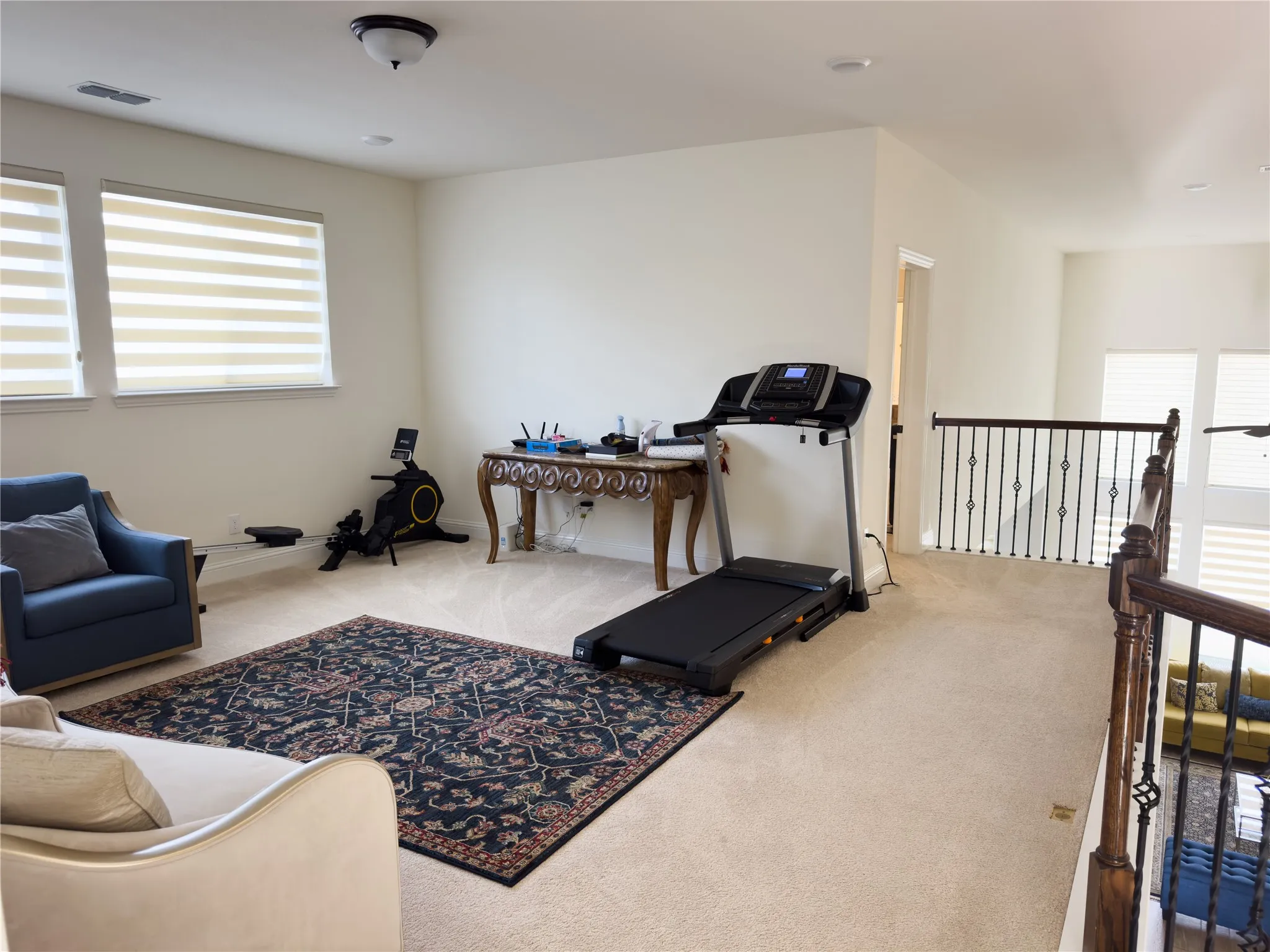 Carpeted room featuring multiple windows with blinds, recessed lighting, and an ornate wrought iron railing