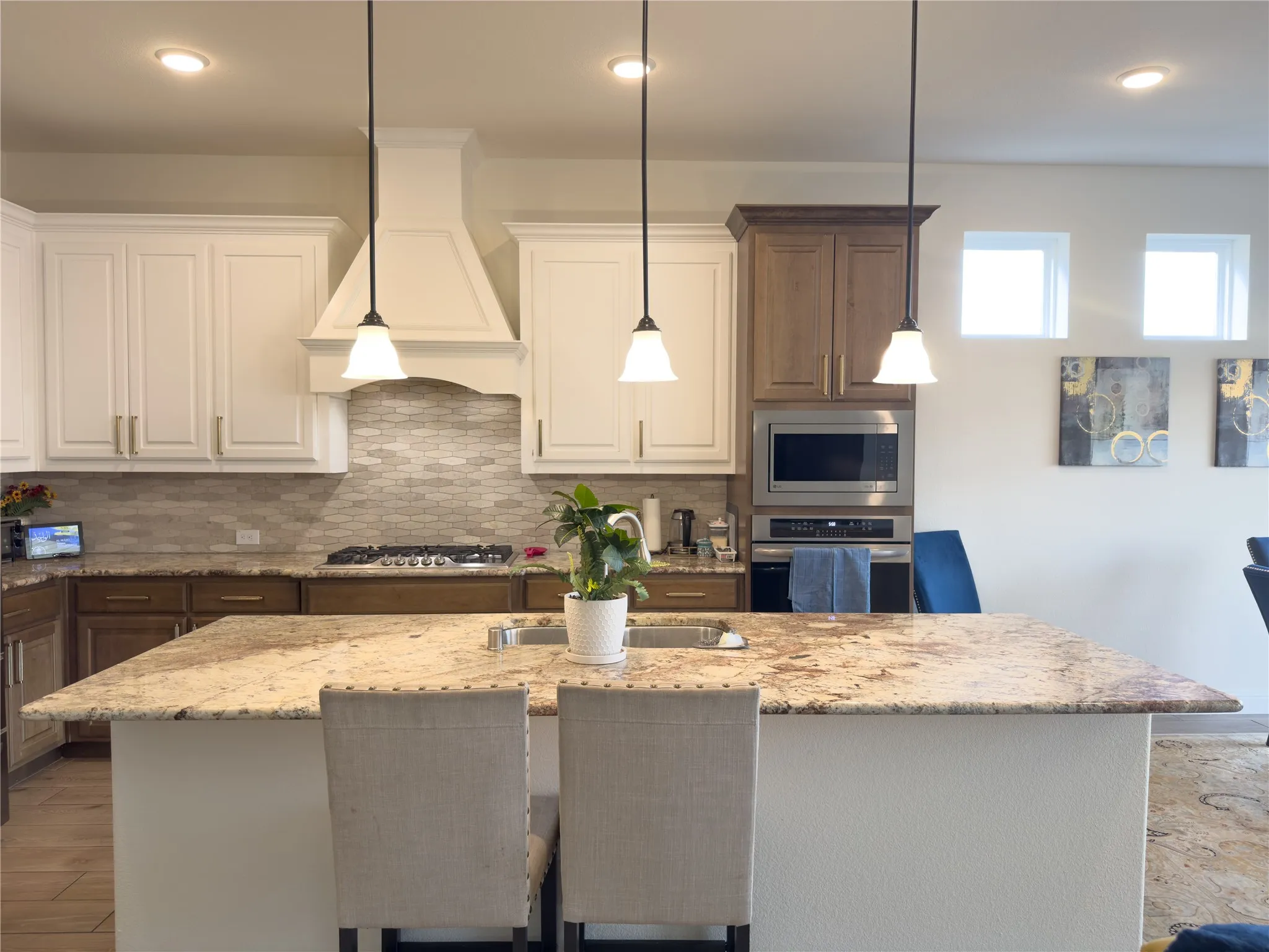 Kitchen featuring a spacious island with a built-in sink, recessed lighting, pendulum lighting fixtures, wood-finish flooring, and stainless steel appliances