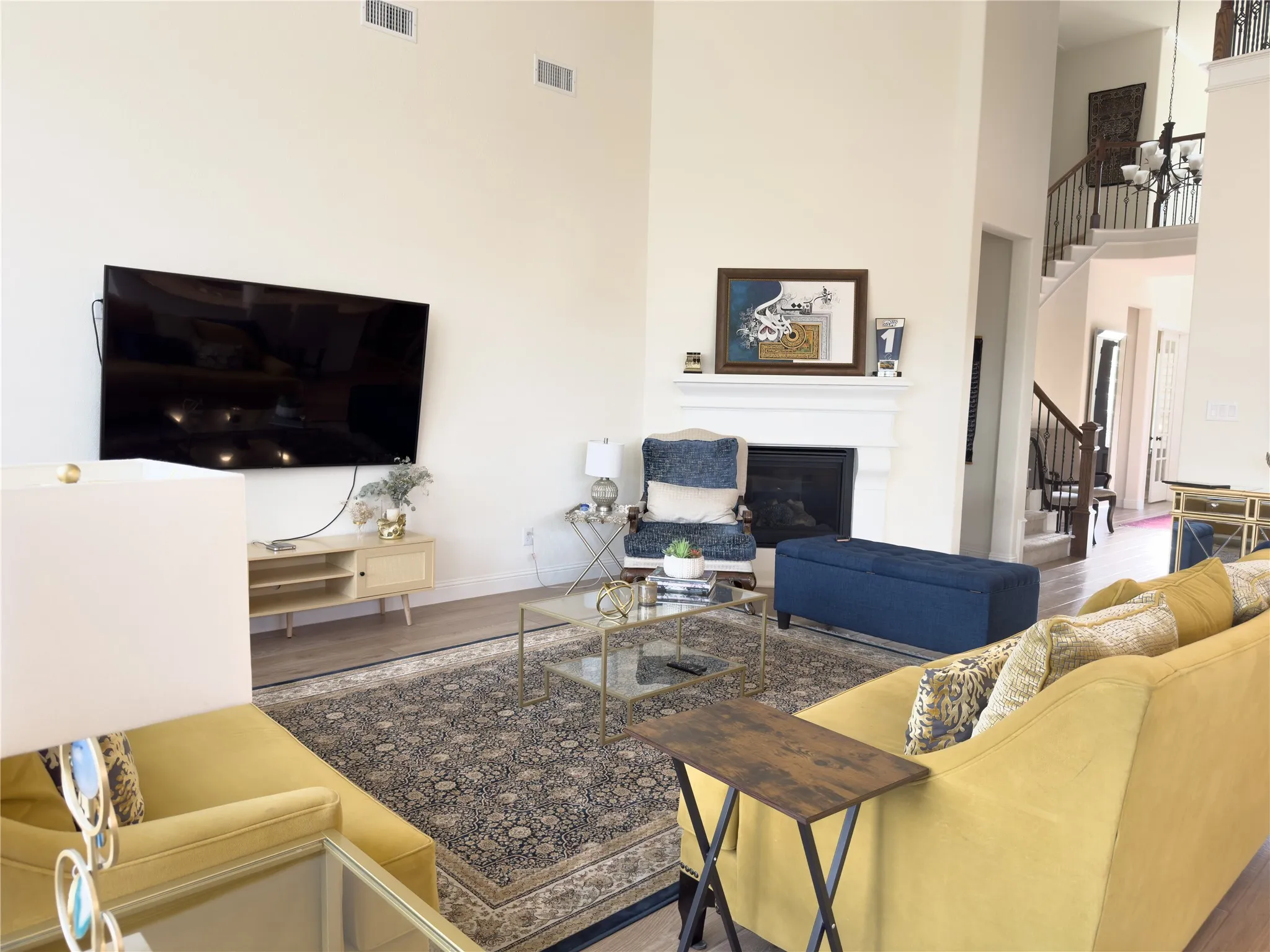 Two-story living room featuring a fireplace with a white mantel, wood-finish flooring, and a staircase with dark wood handrails and balusters
