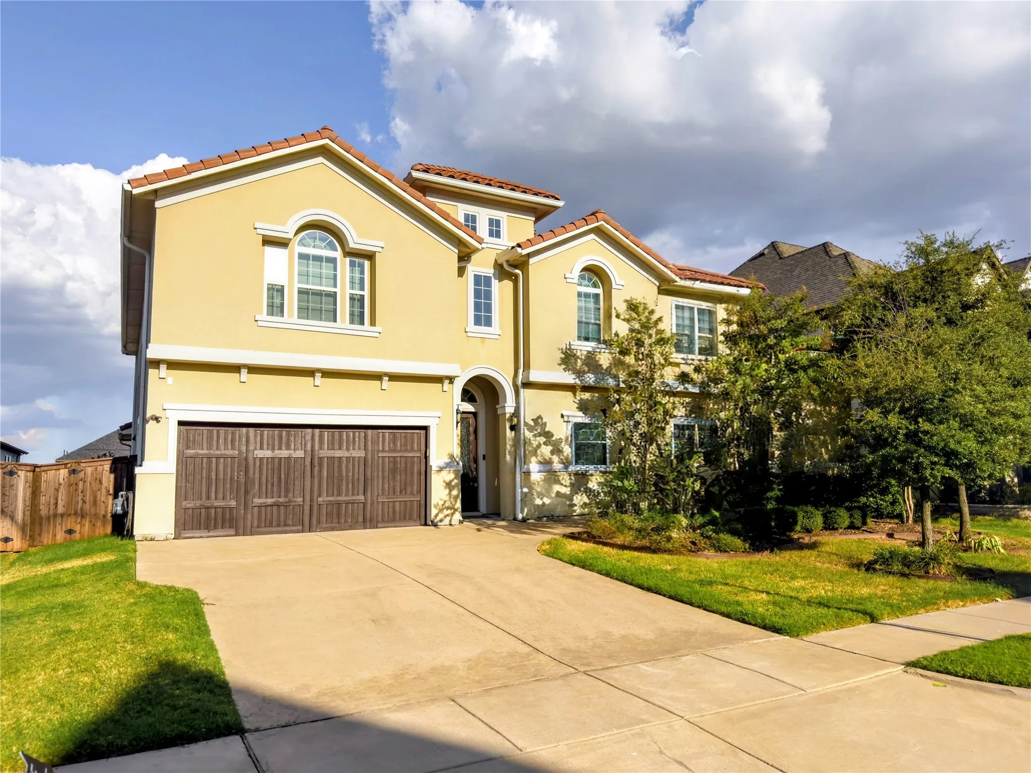 Stucco exterior with arched windows, tile roofing, and a two-car garage with wood-finish doors