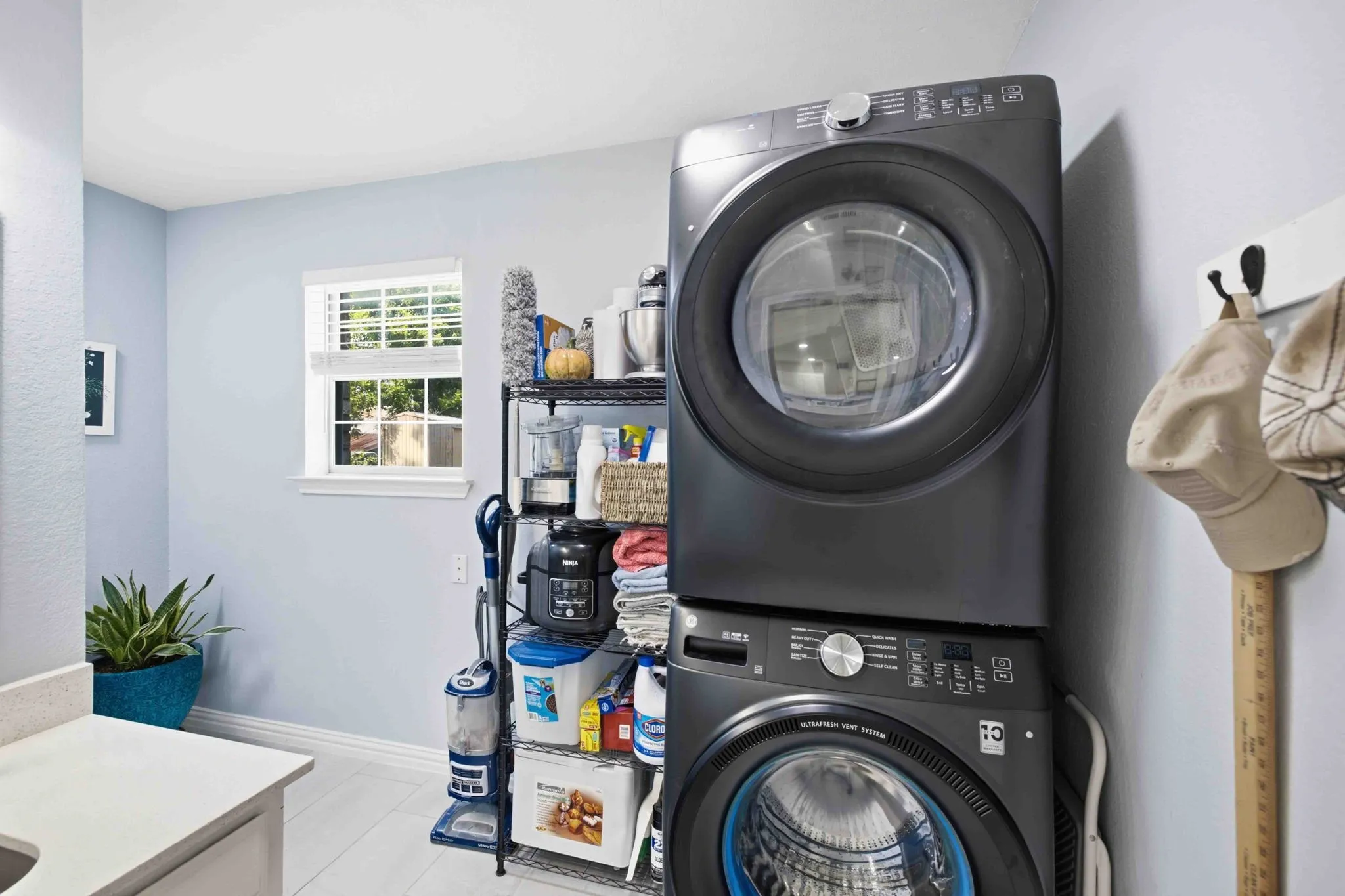 Stackable washer and dryer unit, white window trim, light blue wall paint, and white countertop