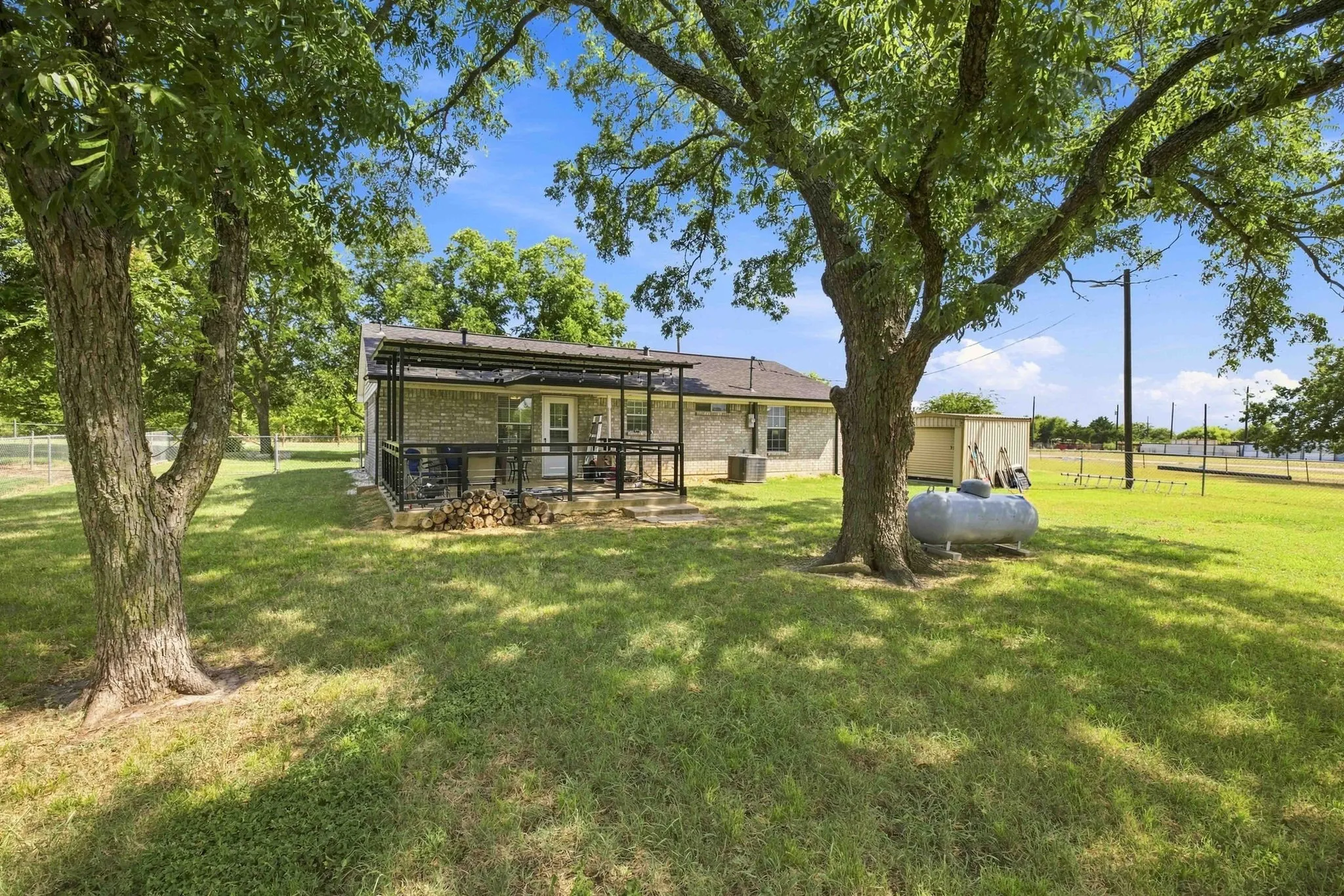 Expansive green lawn with mature trees, a covered patio featuring dark railings, and a storage shed