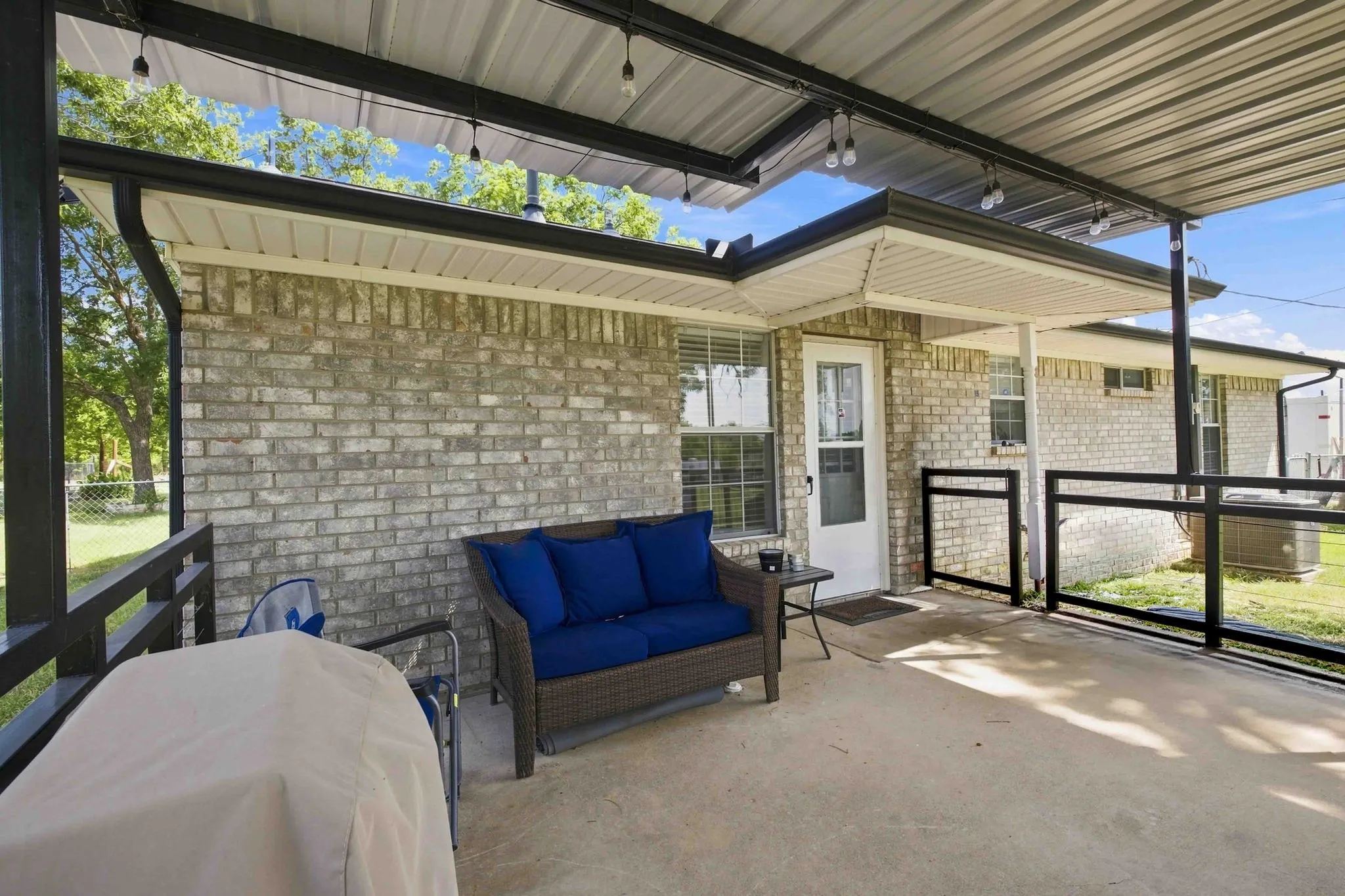 Covered concrete patio featuring string lighting, brick exterior, and black metal railings