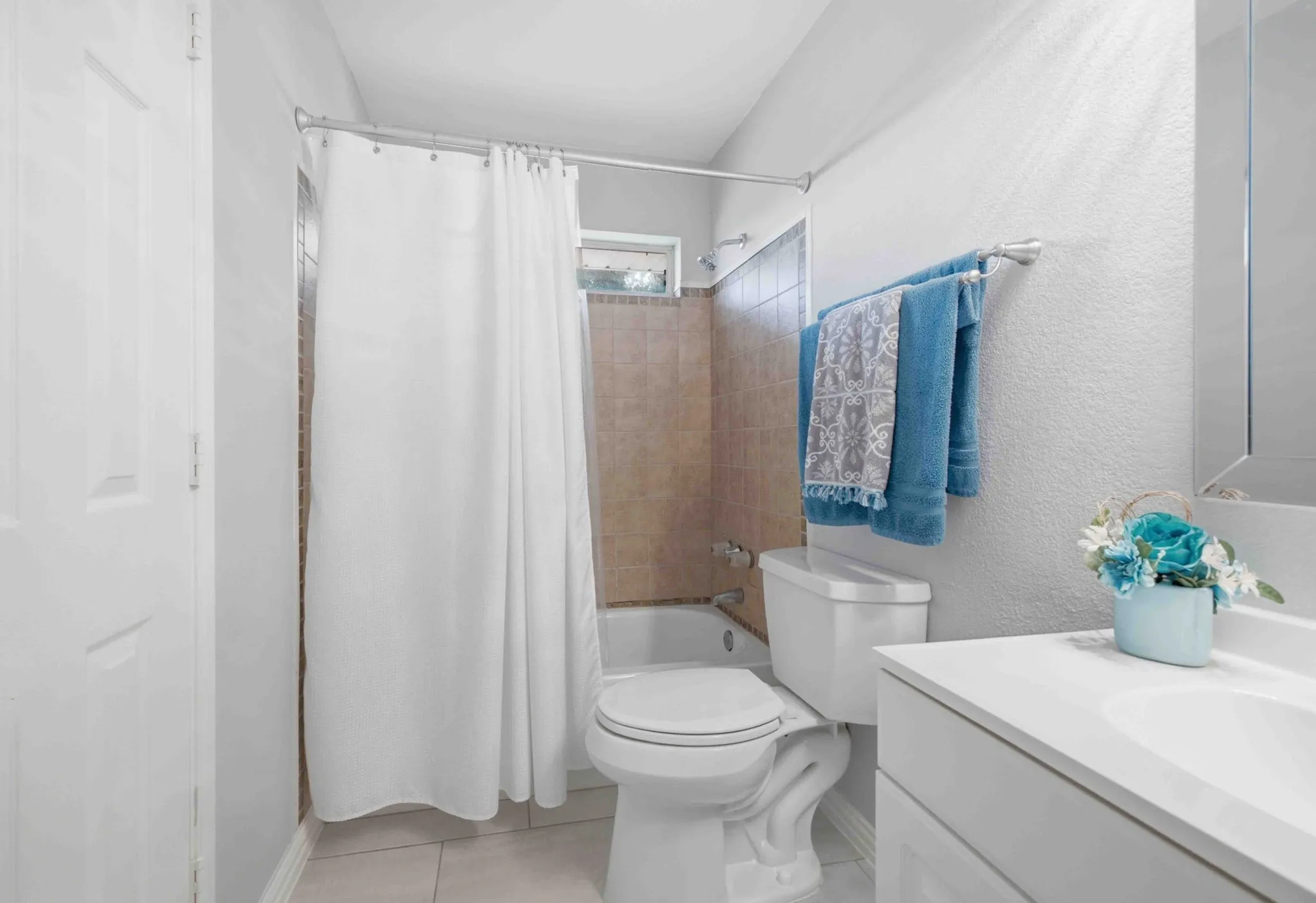 White vanity with integrated sink, white toilet, and tub with tiled surround