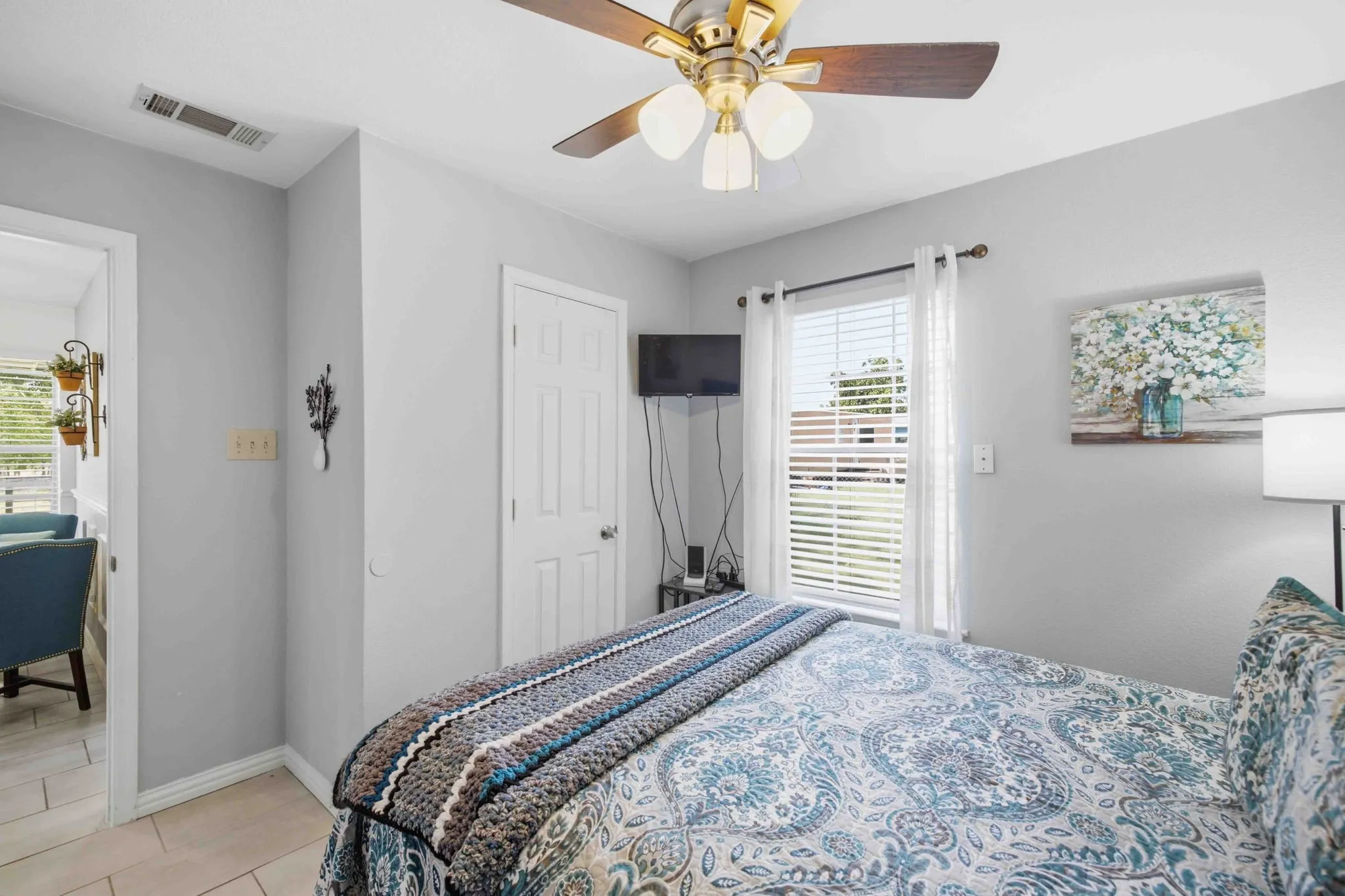 Ceiling fan with light fixture, window with blinds, light-toned walls, paneled interior door, and tile flooring