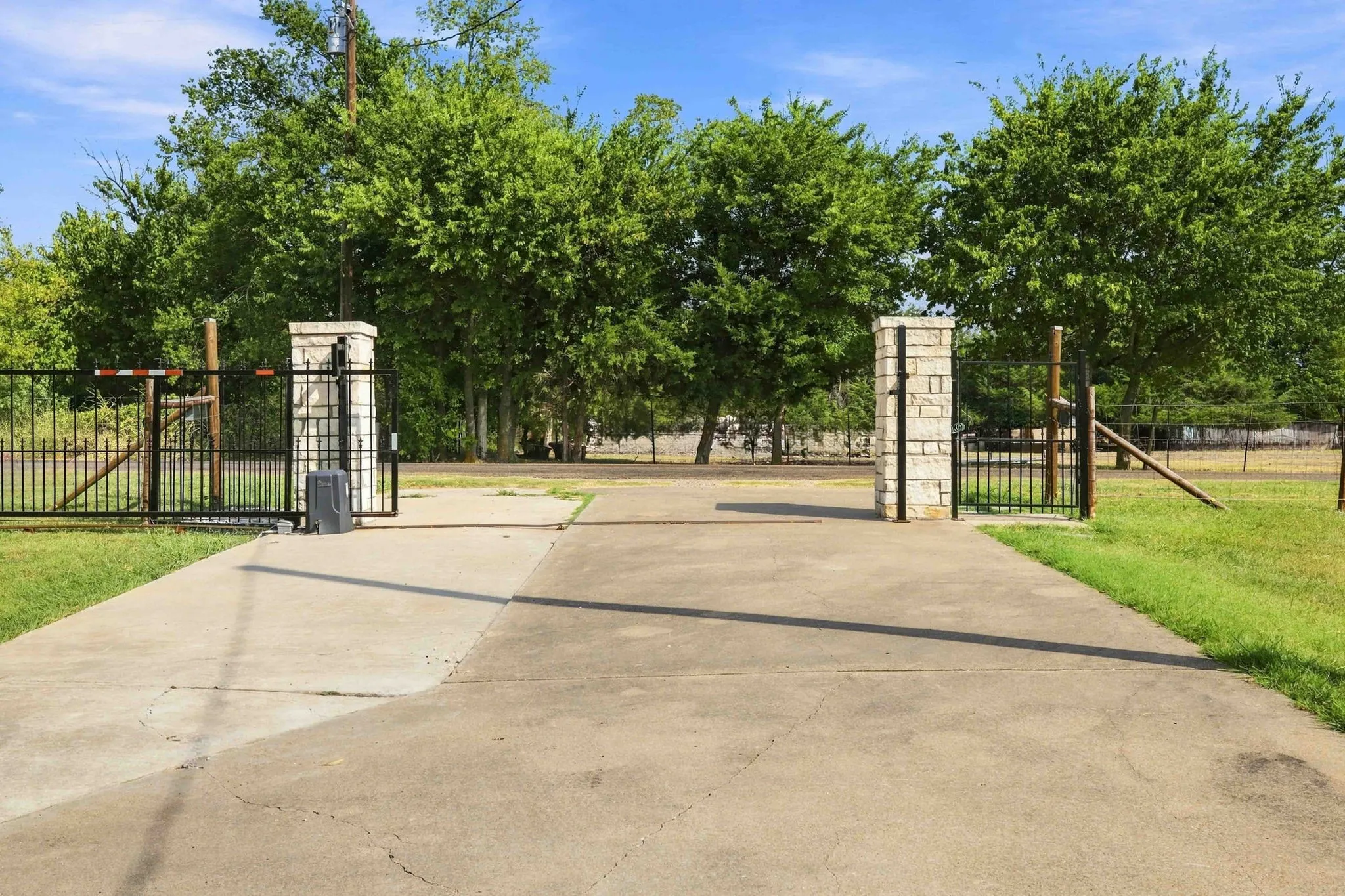 Stone column entrance with an iron gate and concrete driveway