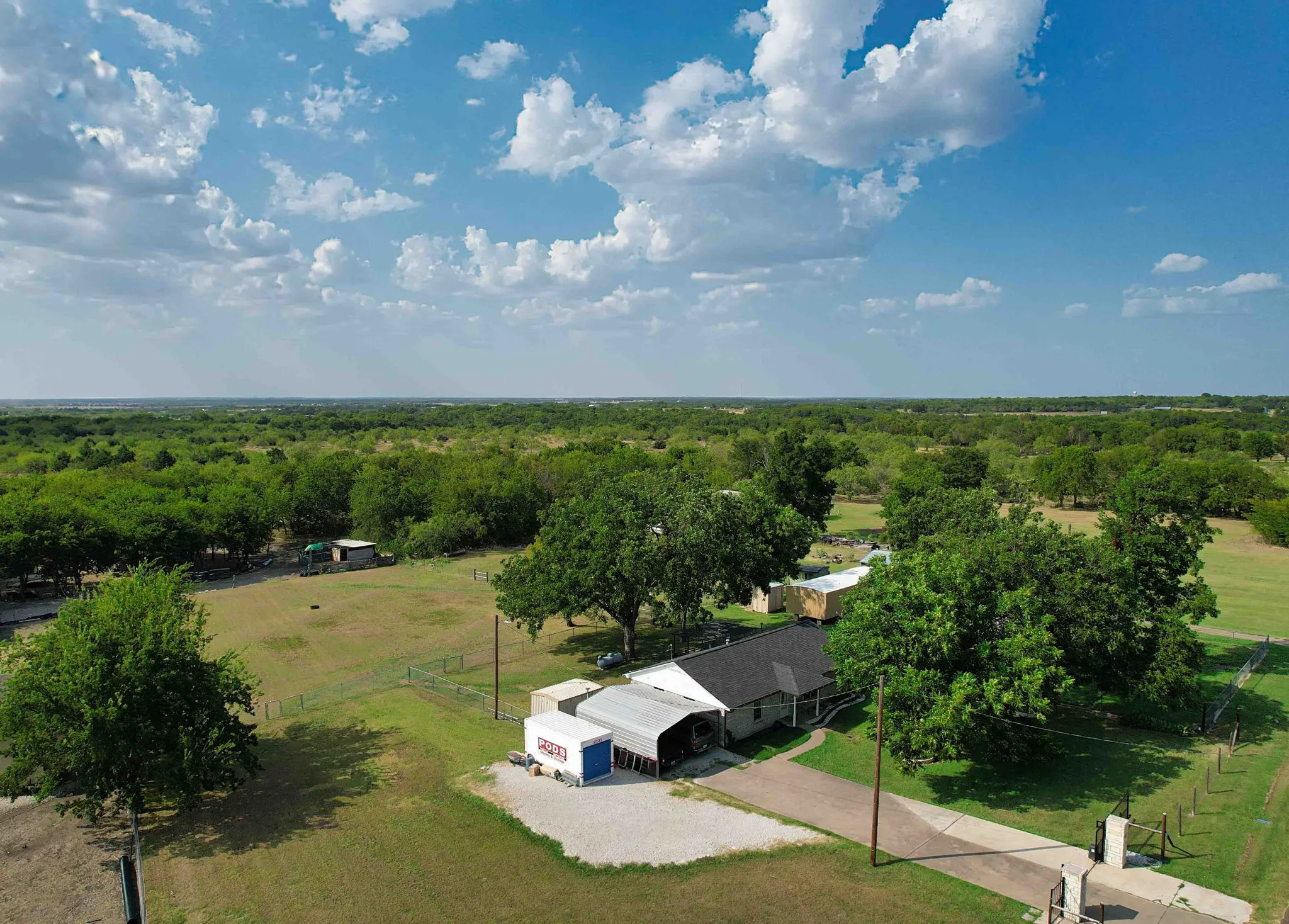 Expansive property with a gravel driveway, mature trees, fencing, and a private entrance gate