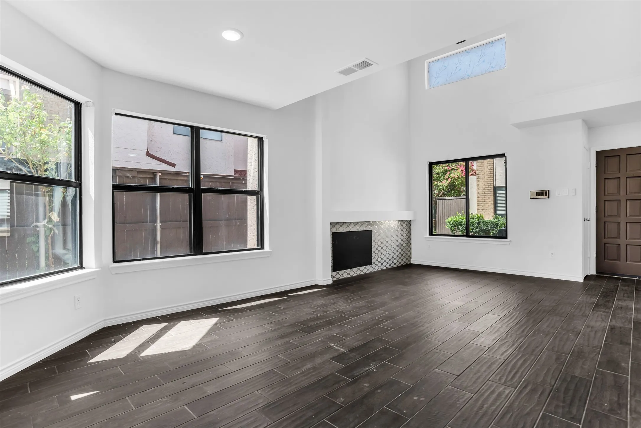 Vaulted ceiling with an upper transom window, recessed lighting, wood-finish flooring, and a fireplace with tile surround