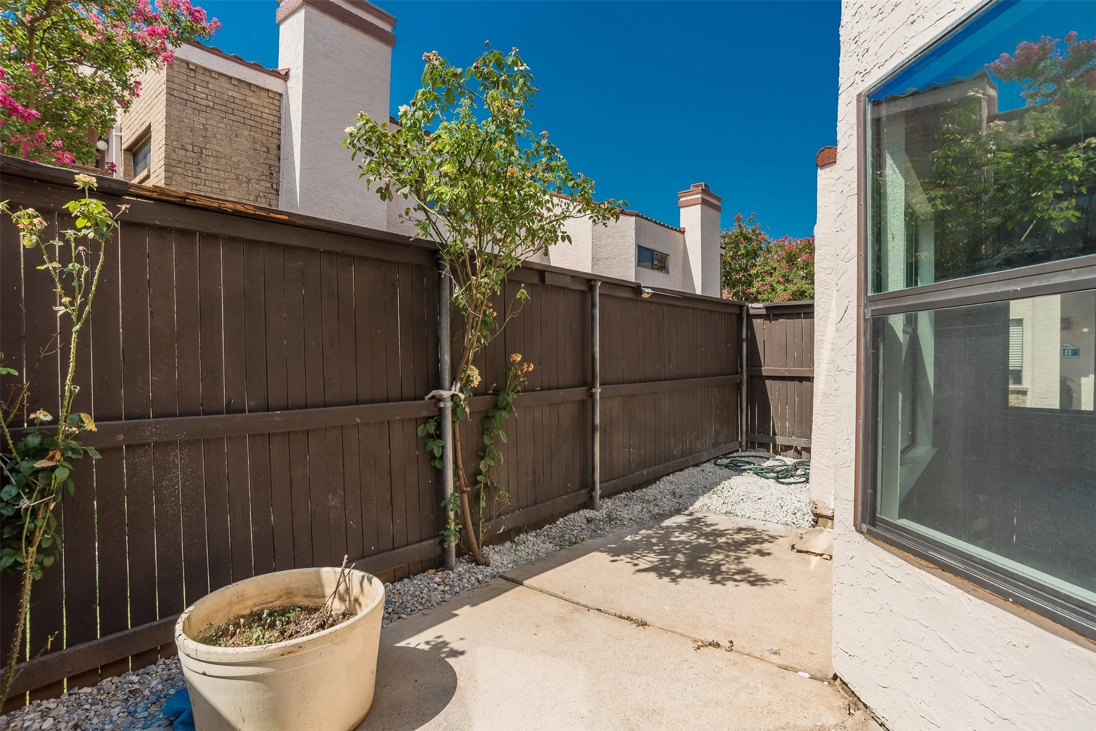 Private concrete patio with gravel landscaping, featuring a tall wood fence and a large window