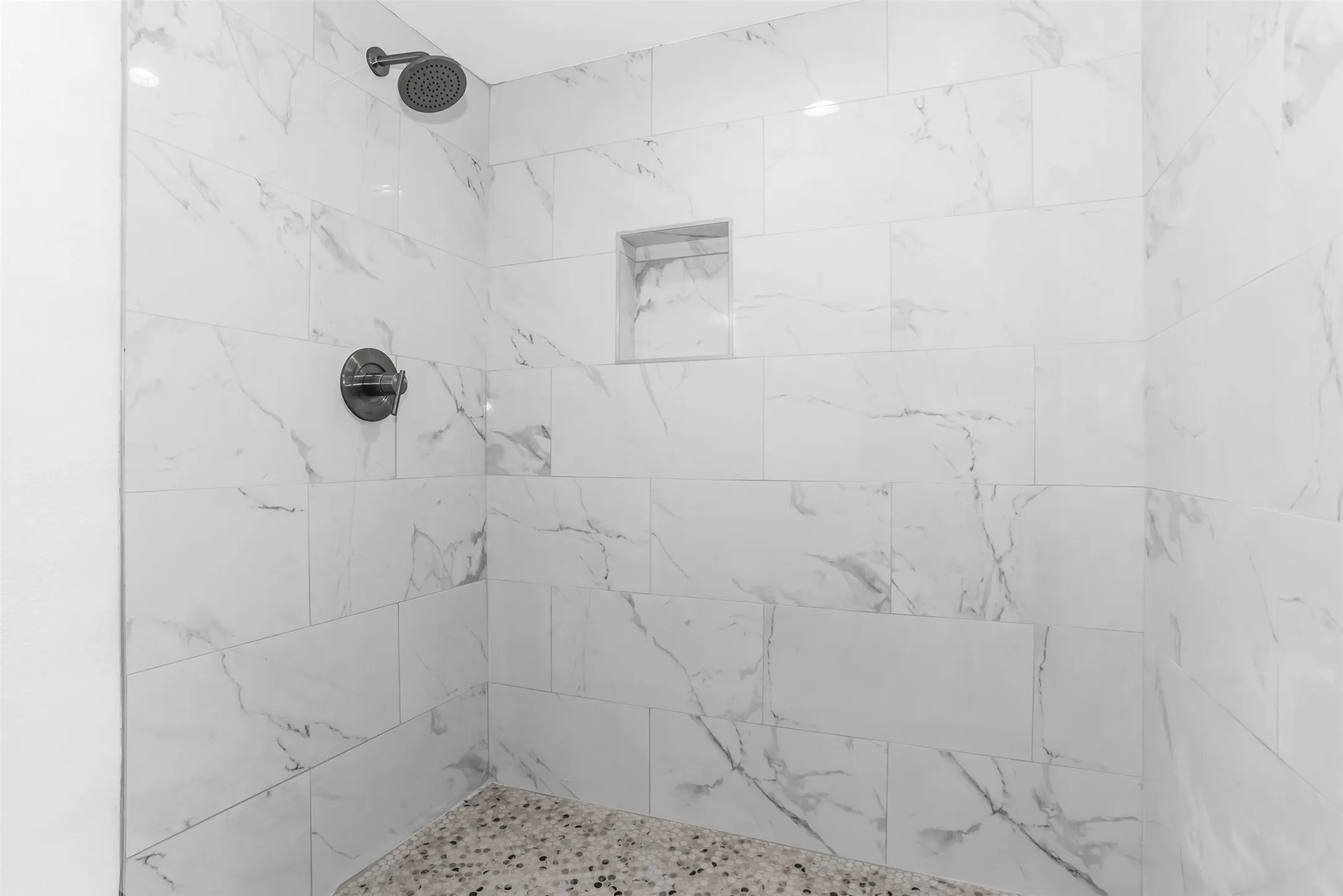 Walk-in shower featuring large format tile, a built-in shower niche, and a contrasting stone mosaic shower pan