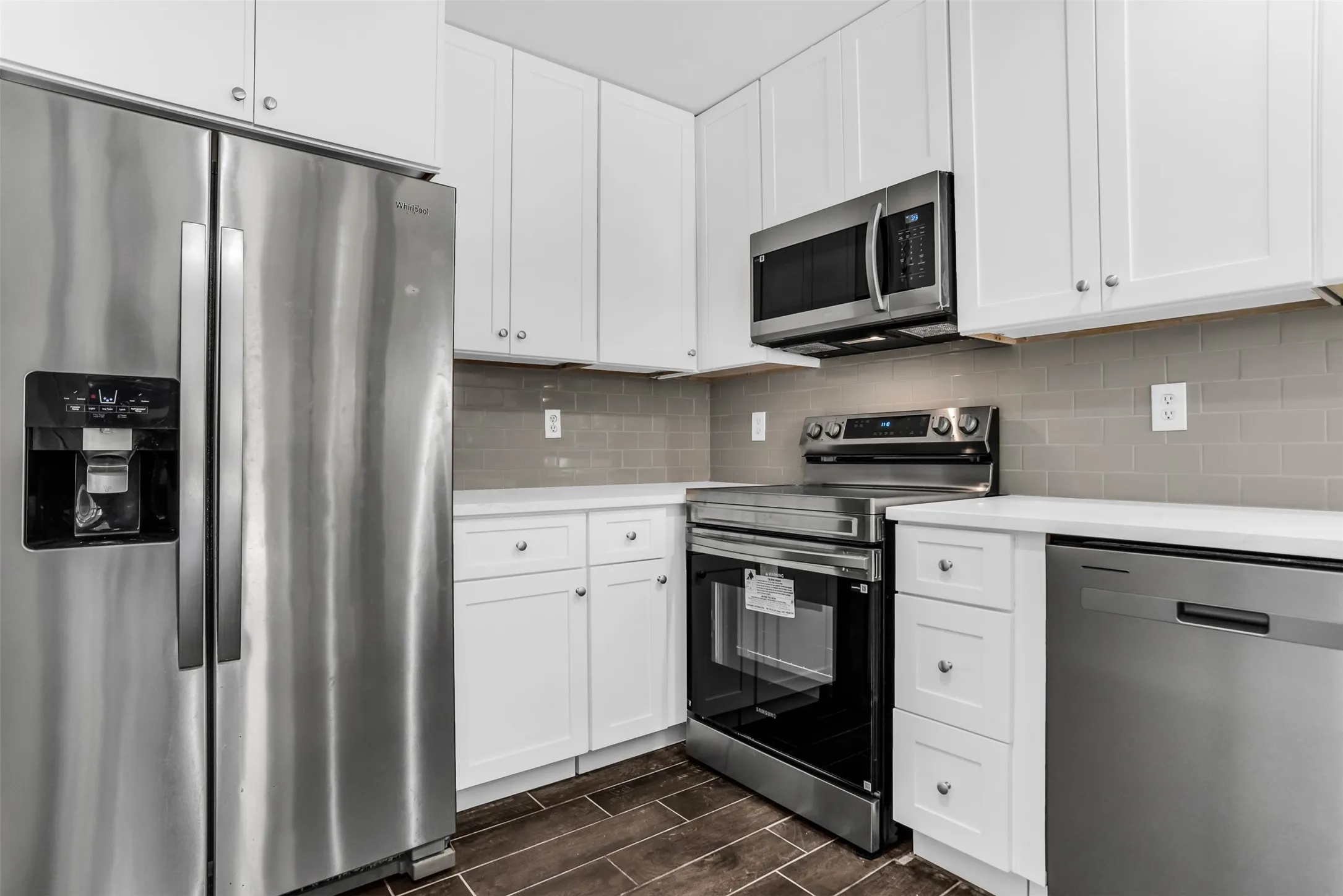 Modern kitchen featuring white cabinetry, stainless steel appliances, light countertops, a subway tile backsplash, and wood-finish flooring