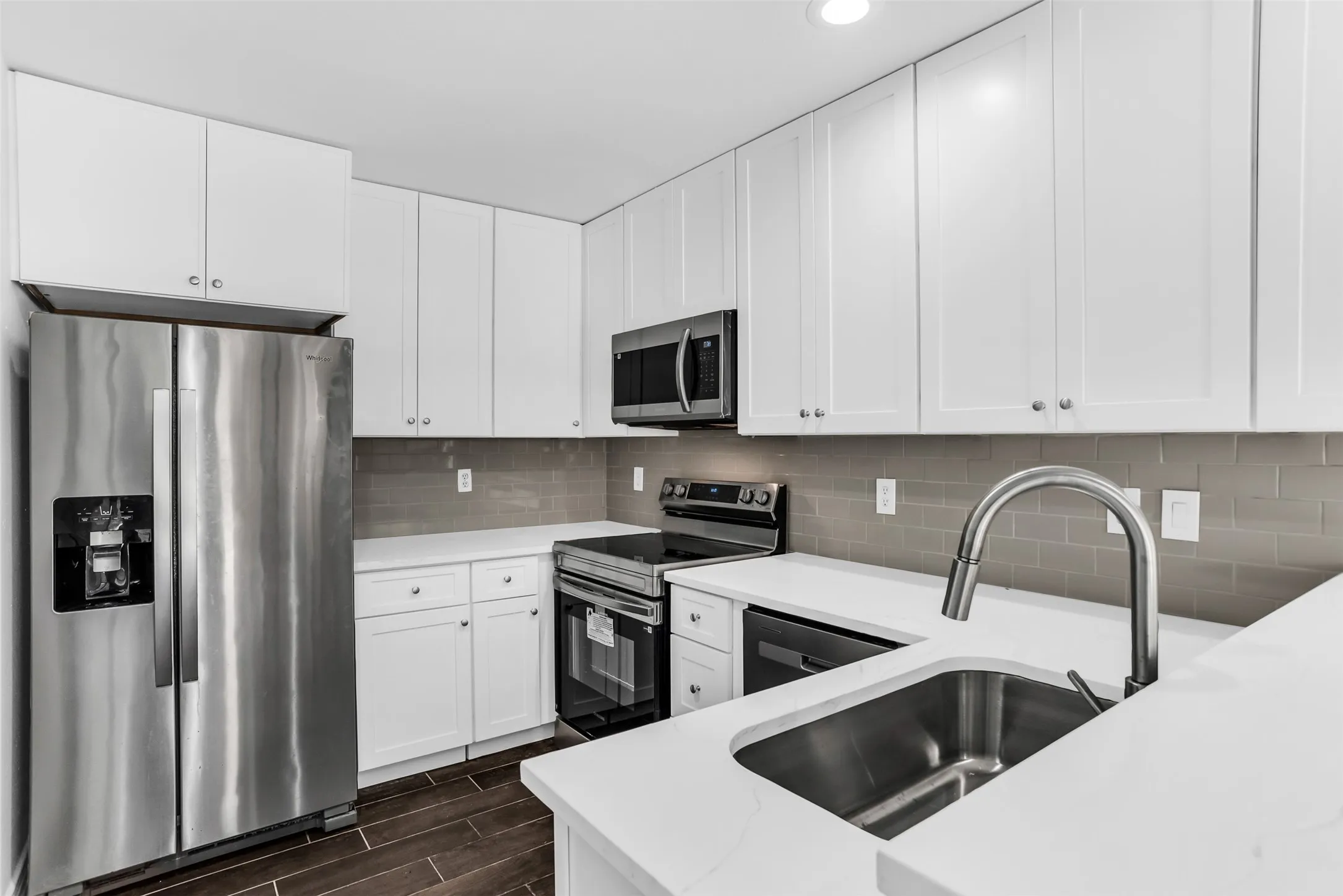 Stainless steel appliances, white cabinetry, neutral subway tile backsplash, white countertops, and wood-finish flooring