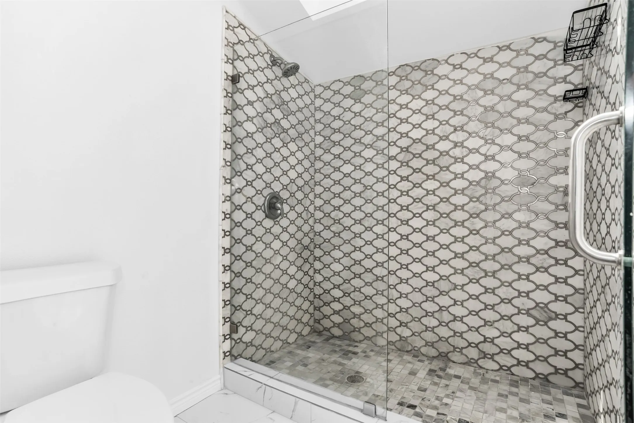Glass-enclosed shower with decorative wall tile, mosaic tile flooring, and a polished chrome showerhead