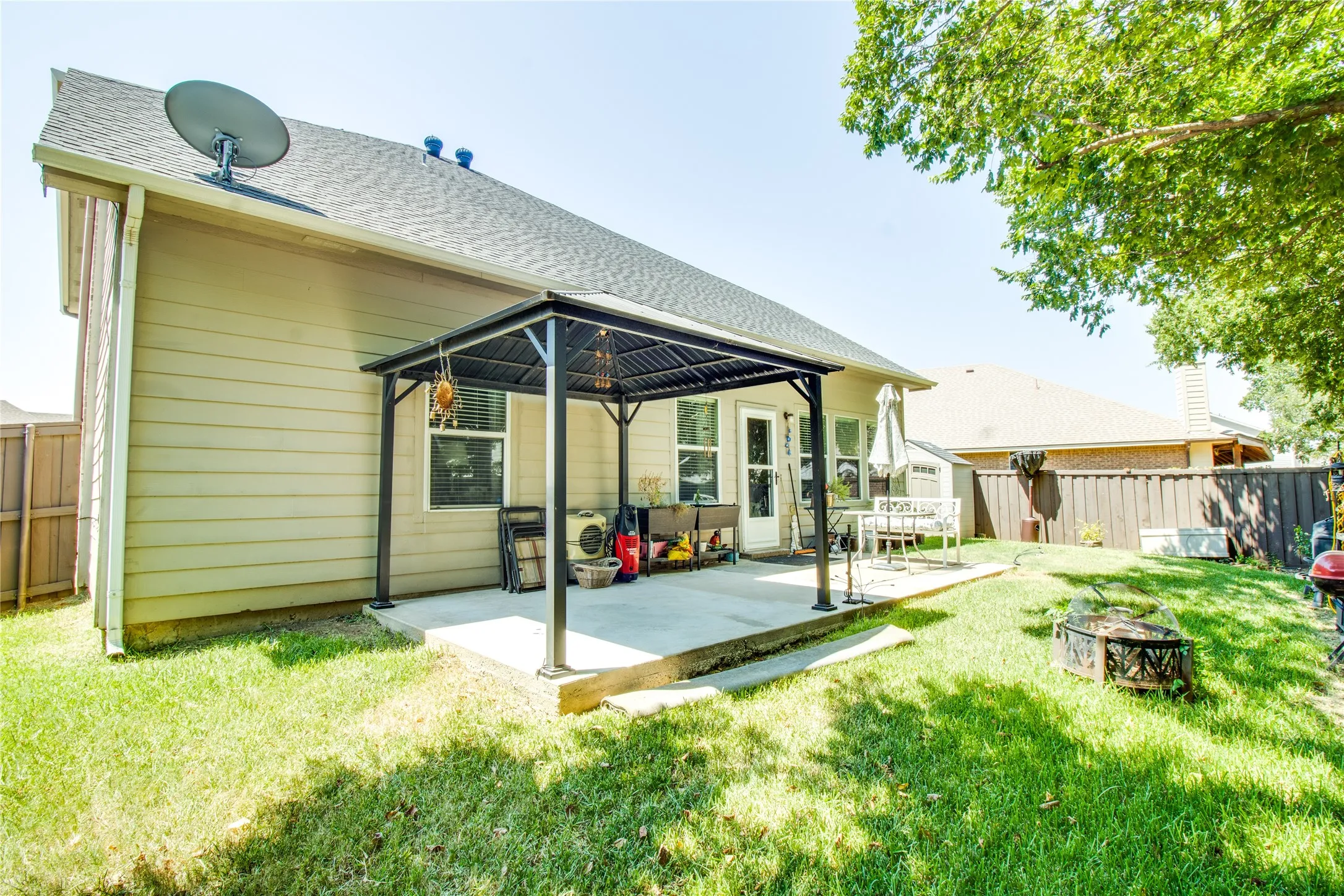 Expansive backyard featuring a concrete patio with a built-in pergola, green lawn space, and a wood privacy fence