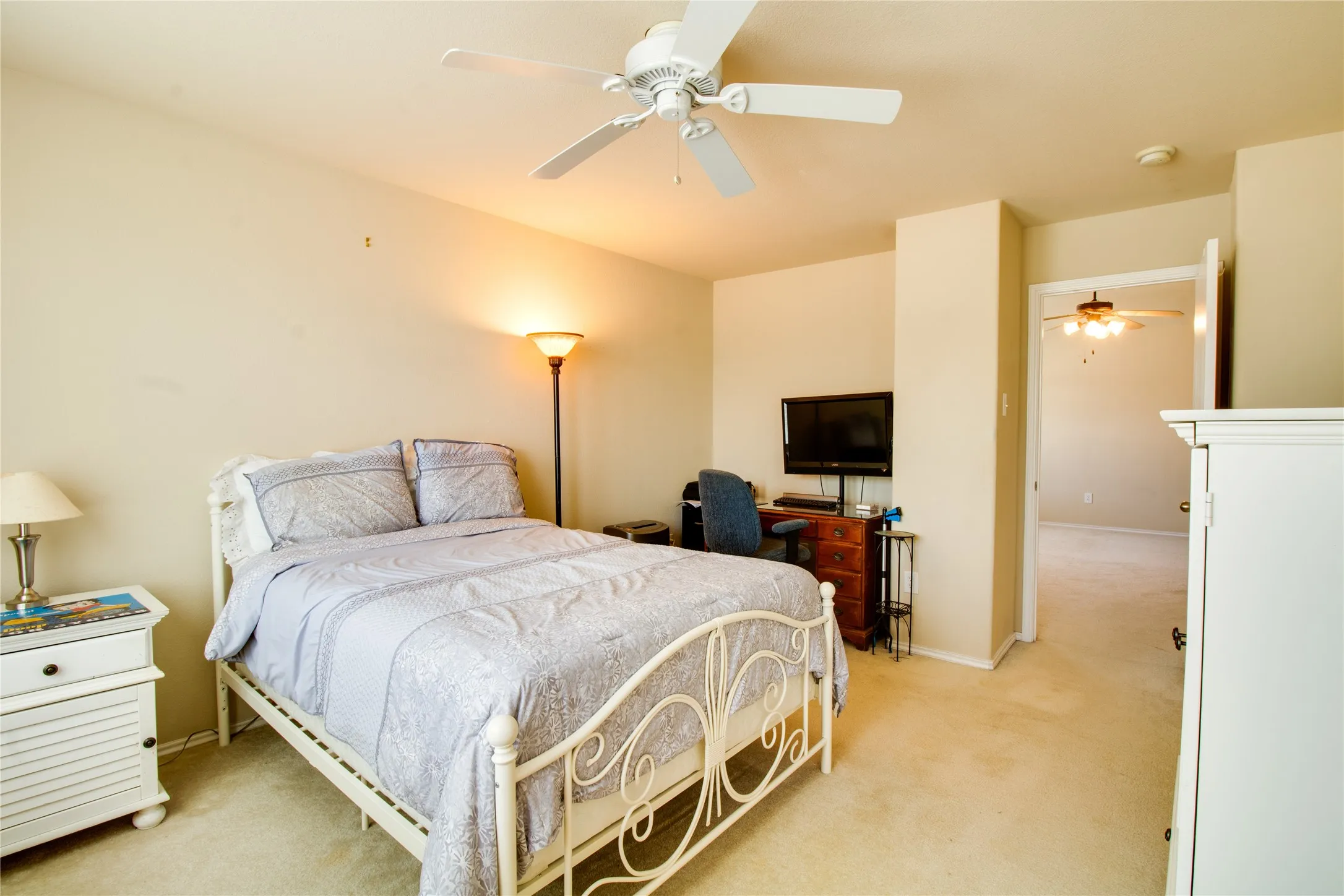 Carpeted bedroom featuring a ceiling fan with light fixture, built-in shelving, and a doorway leading to an additional space