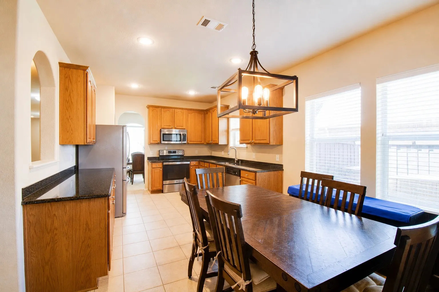 Kitchen and dining area featuring stainless steel appliances, dark stone countertops, wood cabinetry, and tile flooring