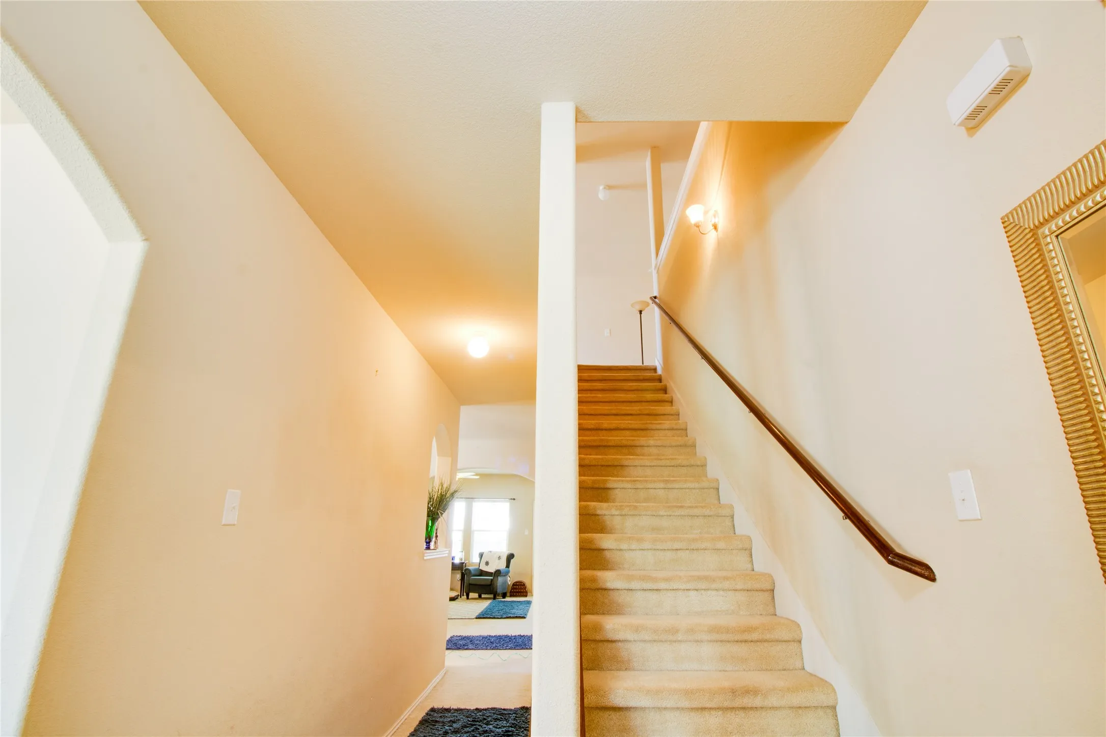 Carpeted staircase with a dark wood handrail and sconce lighting