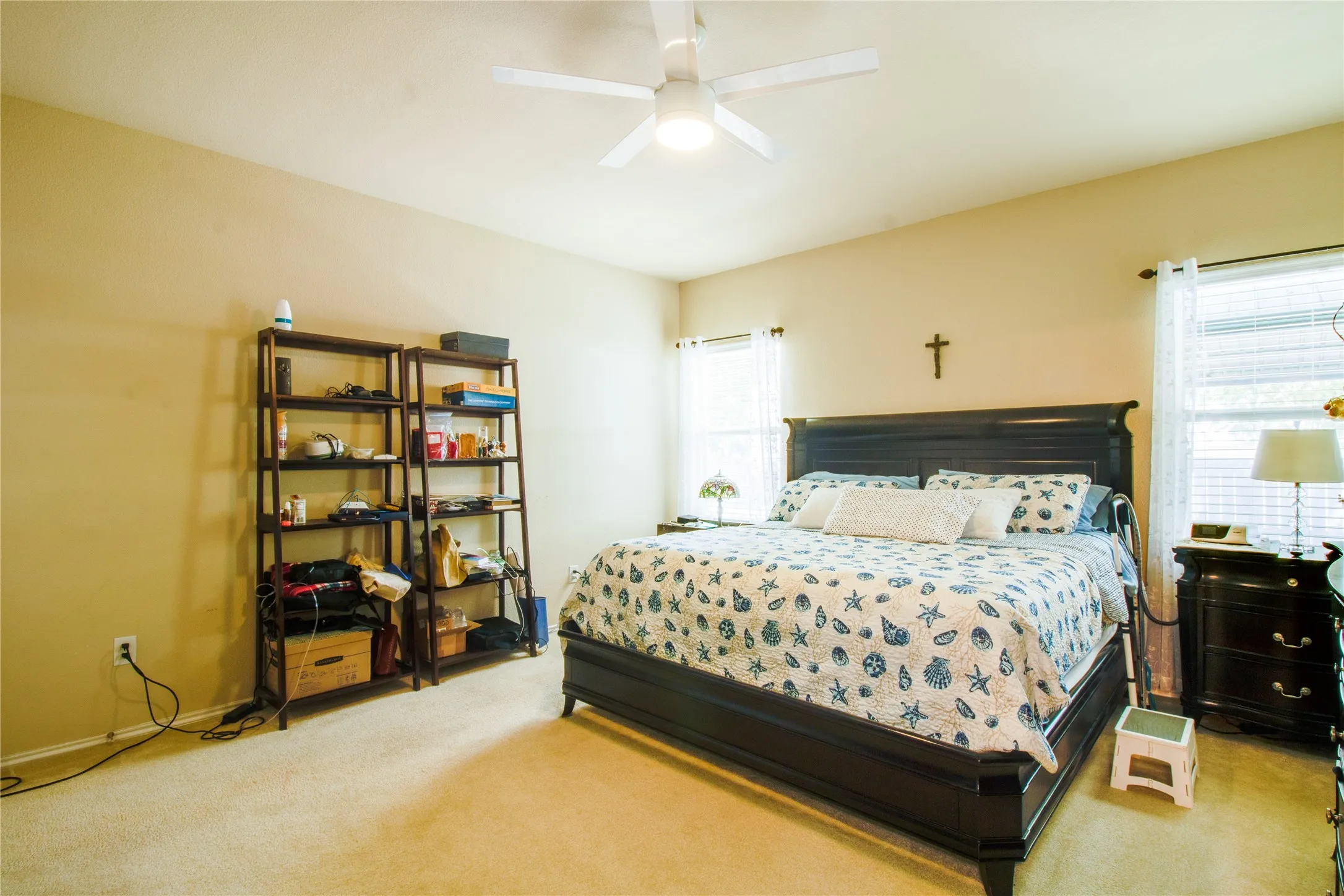 Spacious bedroom featuring neutral wall tones, light-colored carpet, a ceiling fan with integrated lighting, and multiple windows with blinds