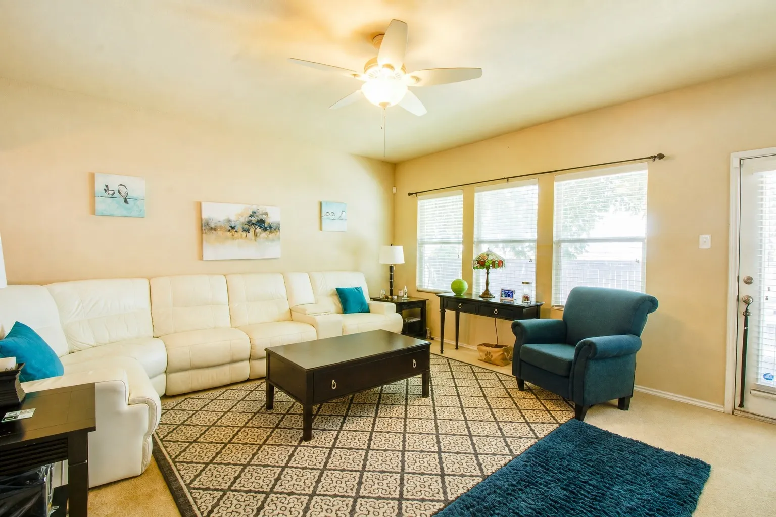 Living area featuring a ceiling fan with integrated lighting, multiple windows with blinds, and a door with an integrated blind