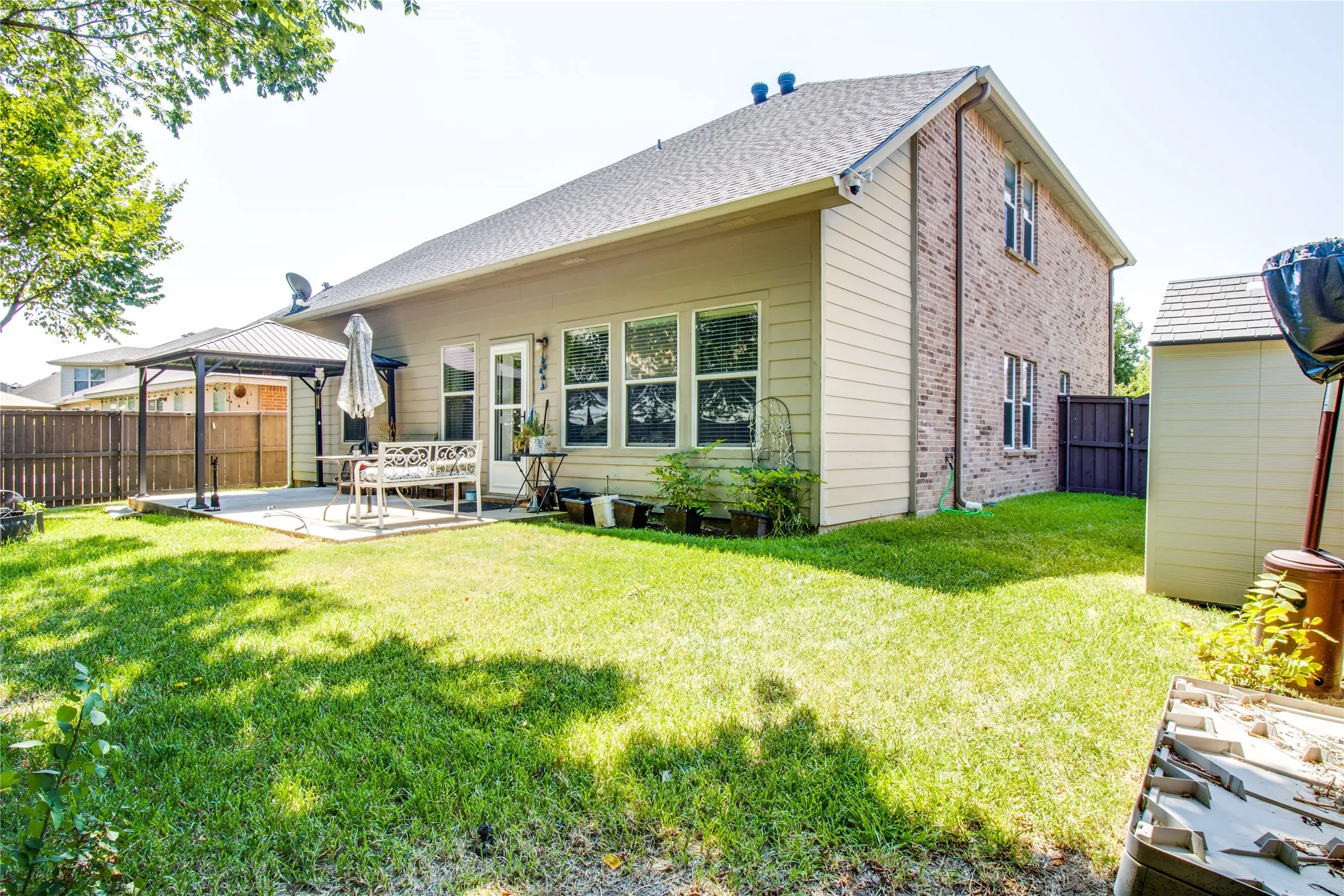Expansive backyard featuring a manicured lawn, concrete patio, privacy fencing, and a detached storage shed