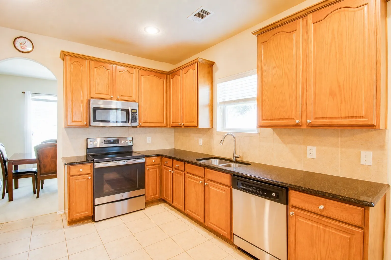 Kitchen featuring wood cabinetry, stainless steel appliances, dark countertops, a tiled backsplash, and tile flooring