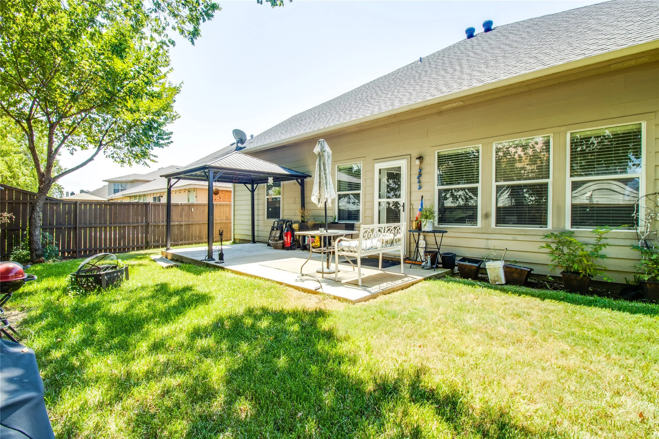 Expansive backyard featuring a concrete patio with a permanent gazebo structure, a wood privacy fence, and mature trees