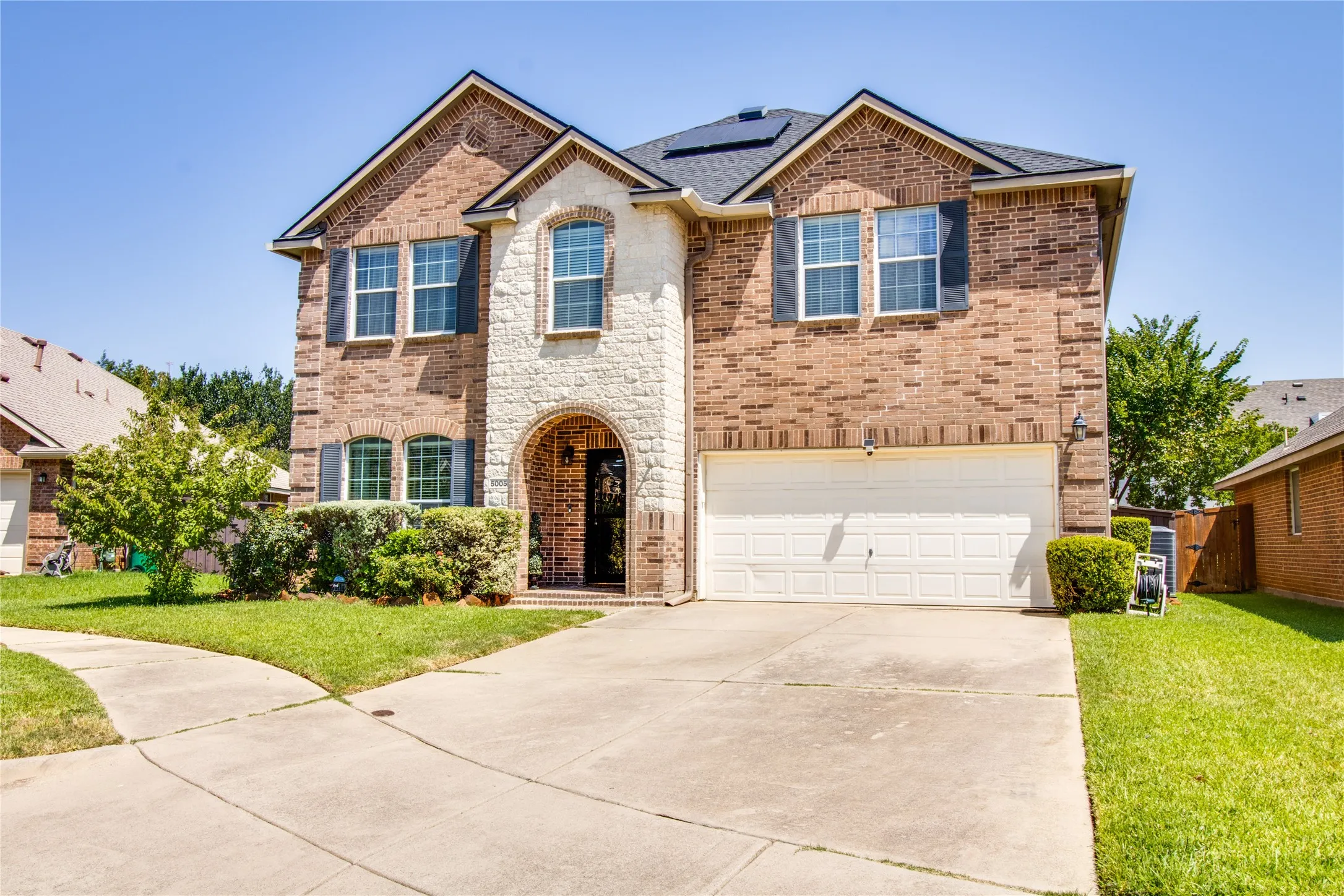 Two-story residence featuring a brick and stone facade with an arched entryway