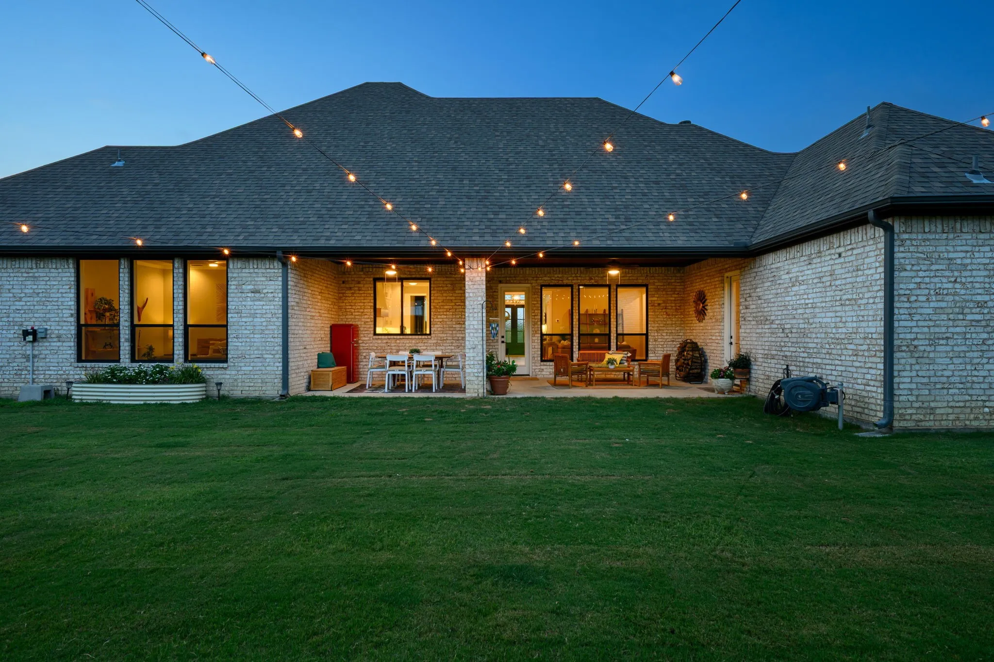 Modern brick residence showcasing an expansive covered patio with French doors, ambient landscape lighting and manicured grounds