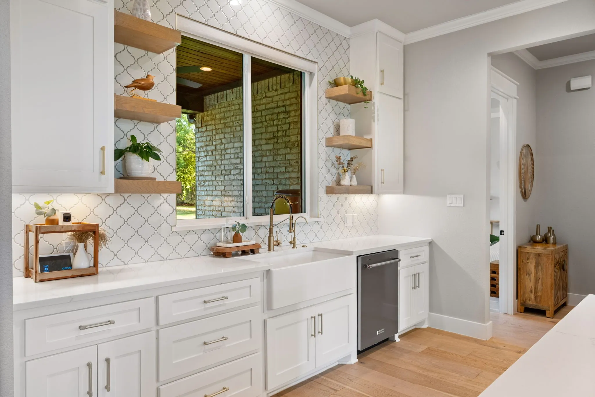 Kitchen featuring a window overlooking a brick patio, a white farmhouse sink, and an integrated dishwasher