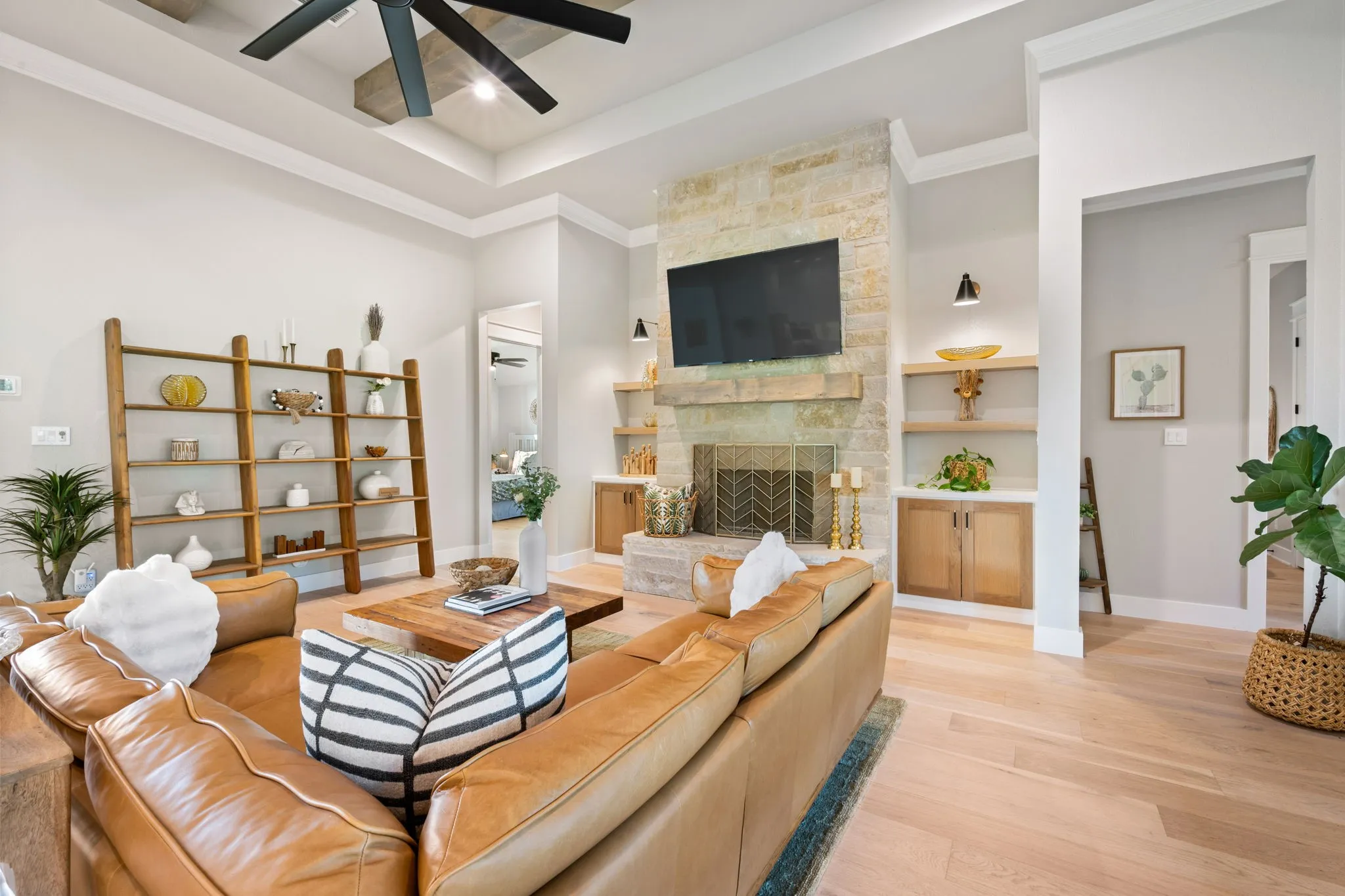 Bright and open living area showcasing wide-plank flooring, a fireplace with stone surround and built-in shelving