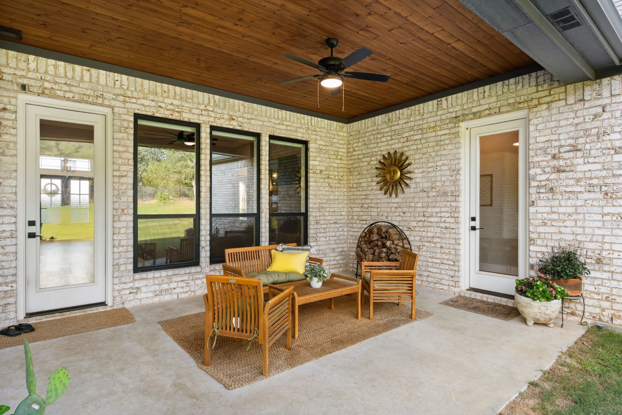 Covered patio featuring a wood-finish ceiling with a ceiling fan, light-colored brick exterior, and multiple full-lite doors and windows