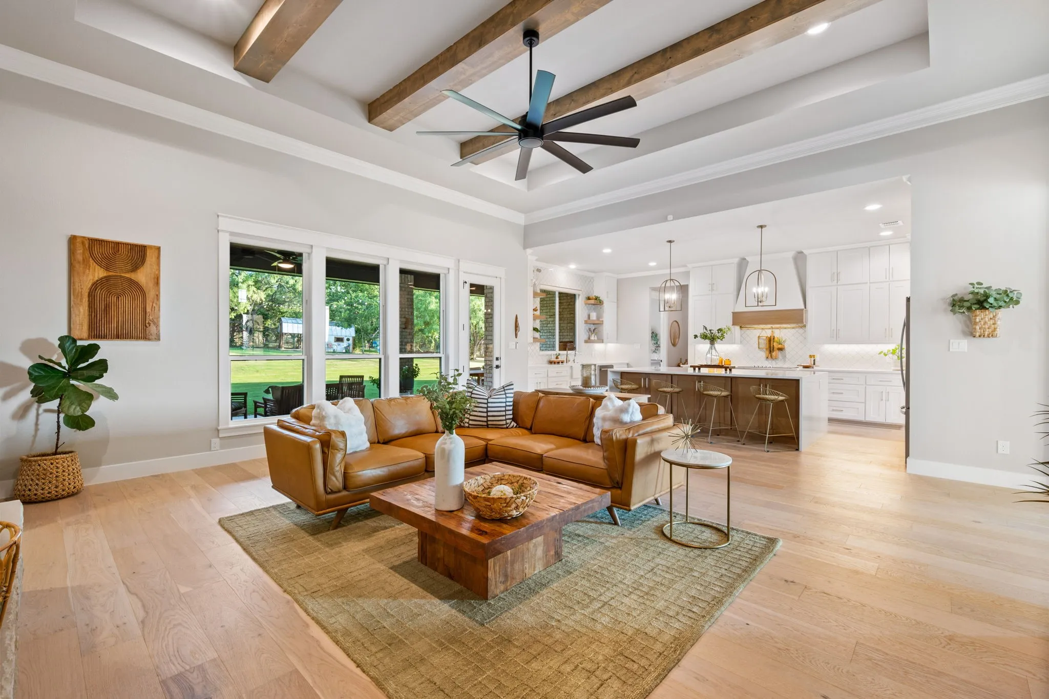 Open-concept living space featuring wide-plank flooring, ceiling with exposed wood beams, and a ceiling fan with integrated lighting