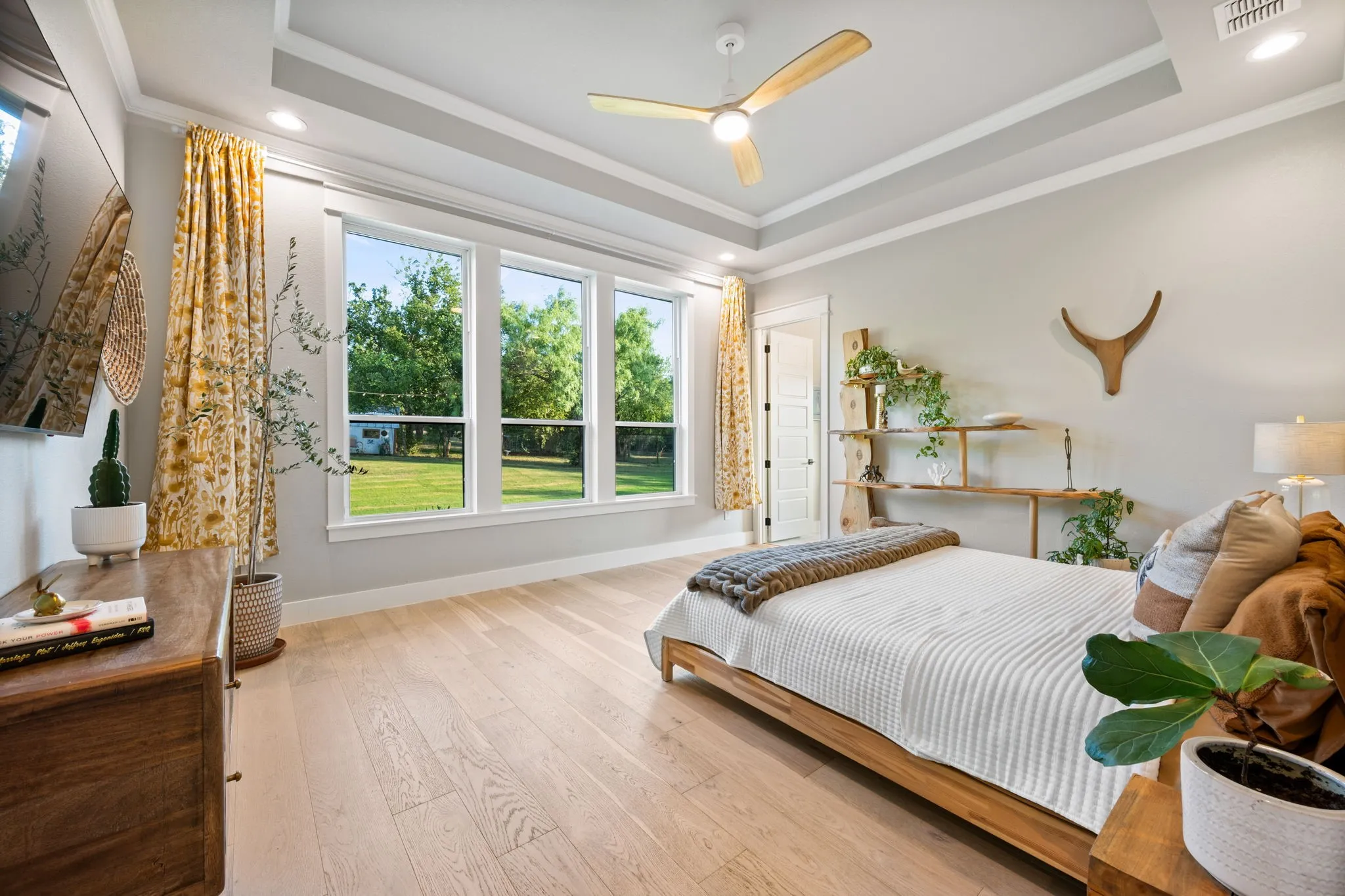 Spacious primary bedroom showcasing a coffered ceiling with ceiling fan and expansive windows framing manicured grounds