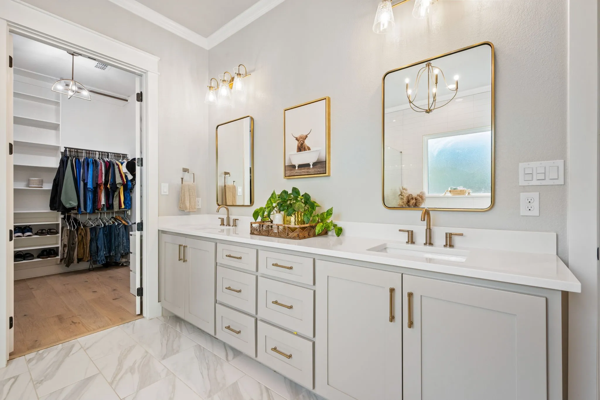Spa-inspired primary bathroom featuring shaker-style vanity with brass hardware, white quartz countertops, and an integrated sinks