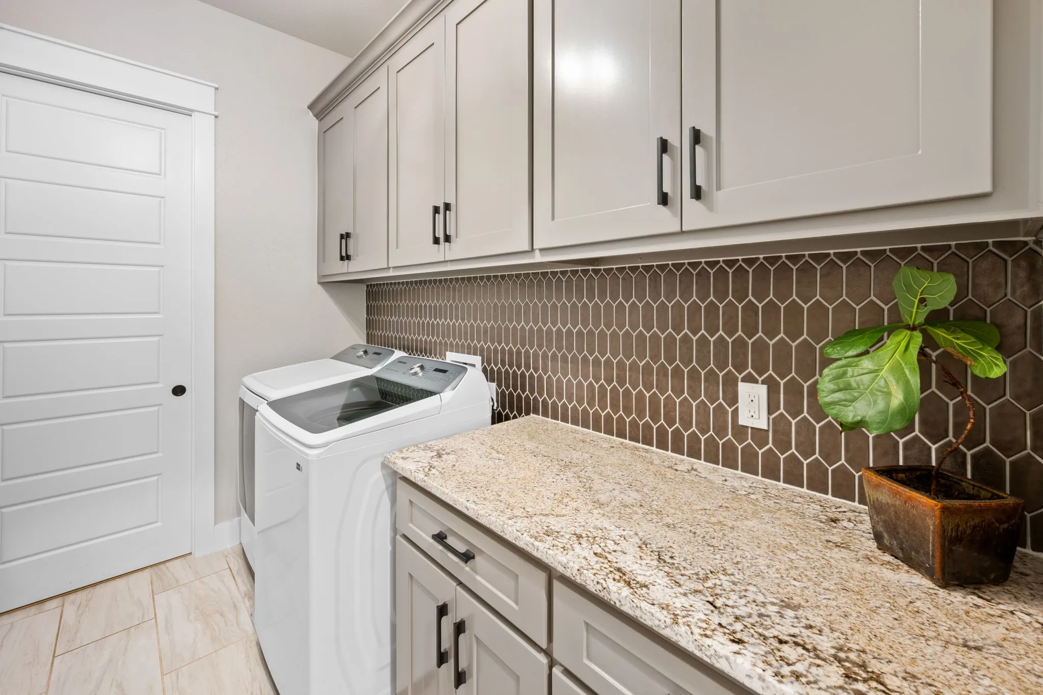 Laundry room featuring white cabinetry with black hardware, granite-look countertops, and a geometric tile backsplash
