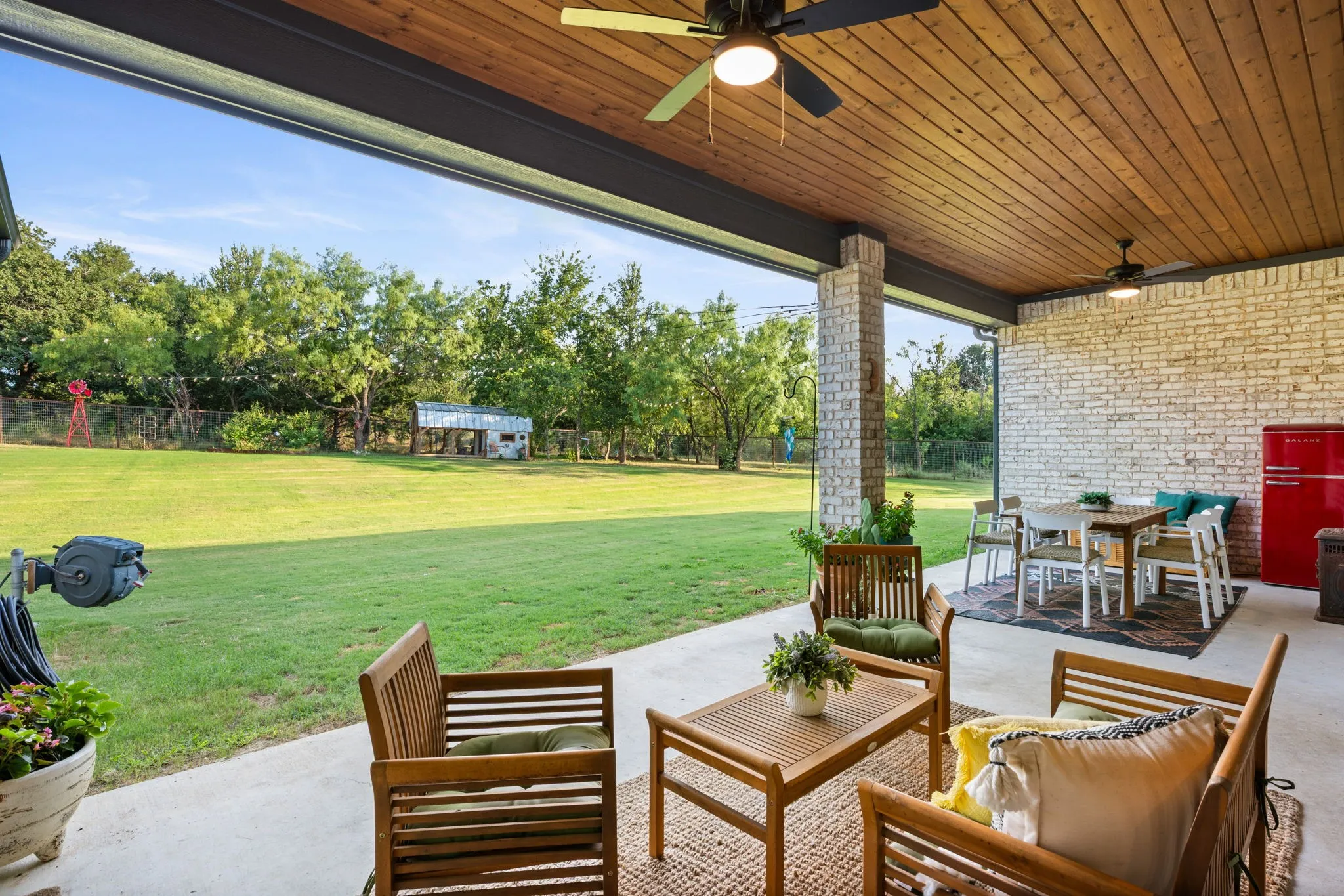 Expansive covered patio featuring a wood-finish ceiling, dual ceiling fans, and a light-colored brick accent wall