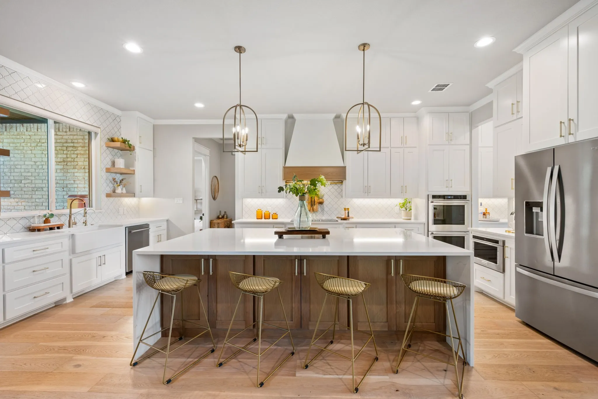 Chef's kitchen featuring white cabinetry, a large waterfall-edge island with wood-finish base, quartz countertops, stainless steel appliances including dual wall ovens, and pendant lighting