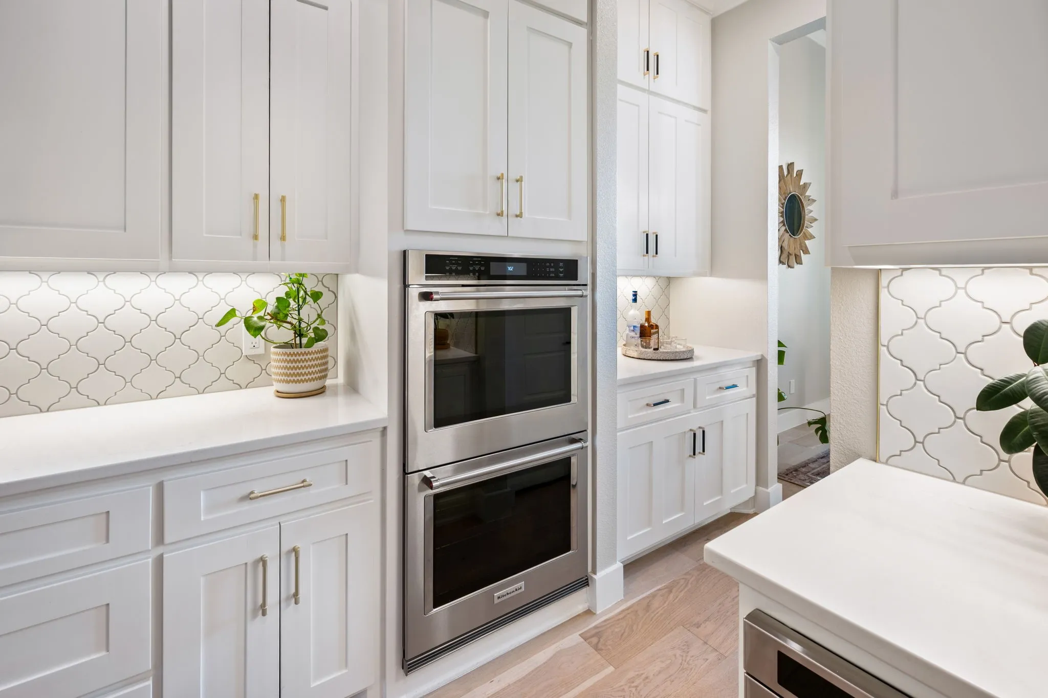 Elegant white cabinetry anchors this chef's kitchen, featuring dual stainless steel wall ovens, quartz countertops, and a geometric tile backsplash