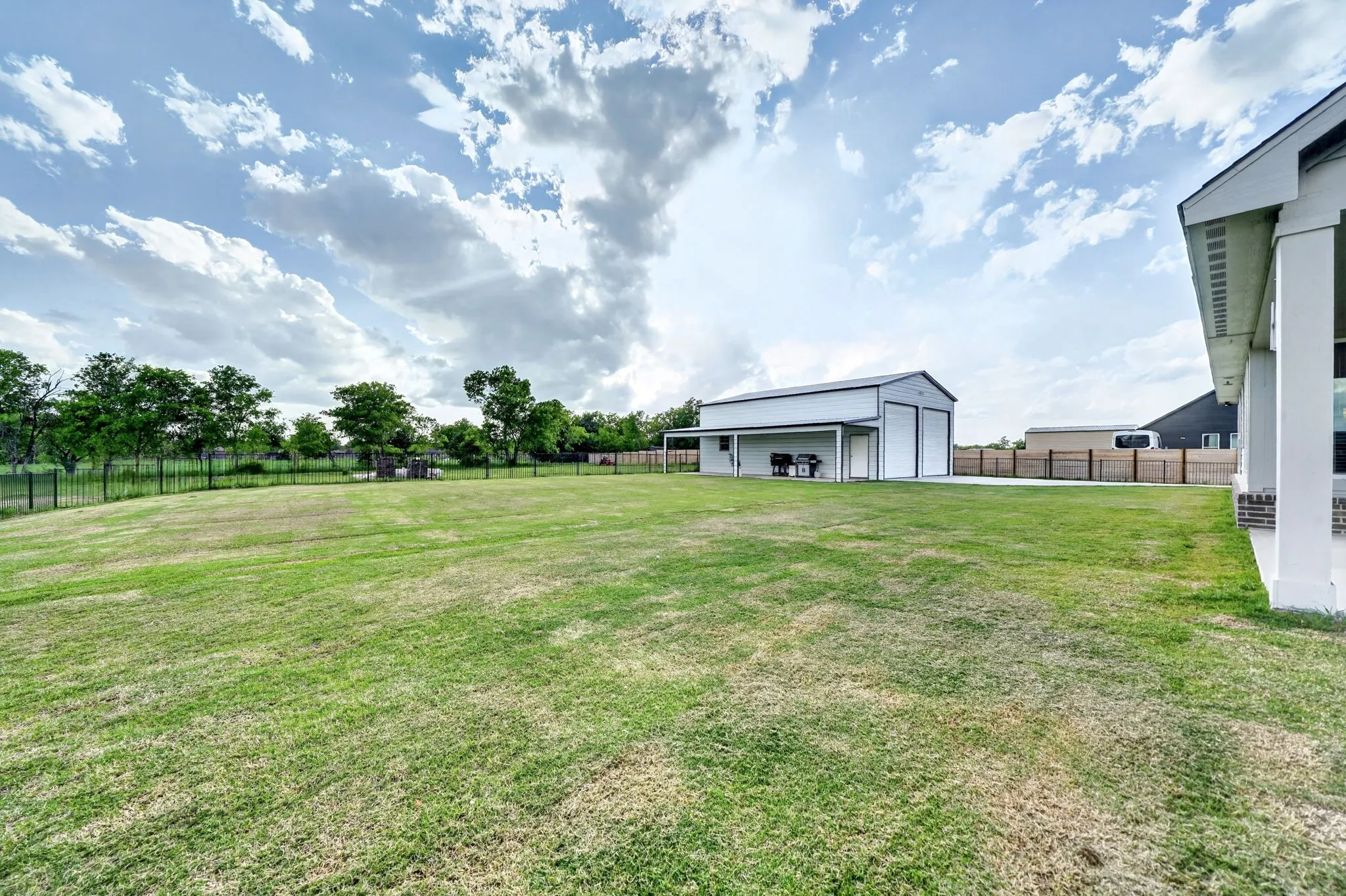 Expansive grassy yard area with a detached outbuilding featuring two garage doors and an extended covered patio