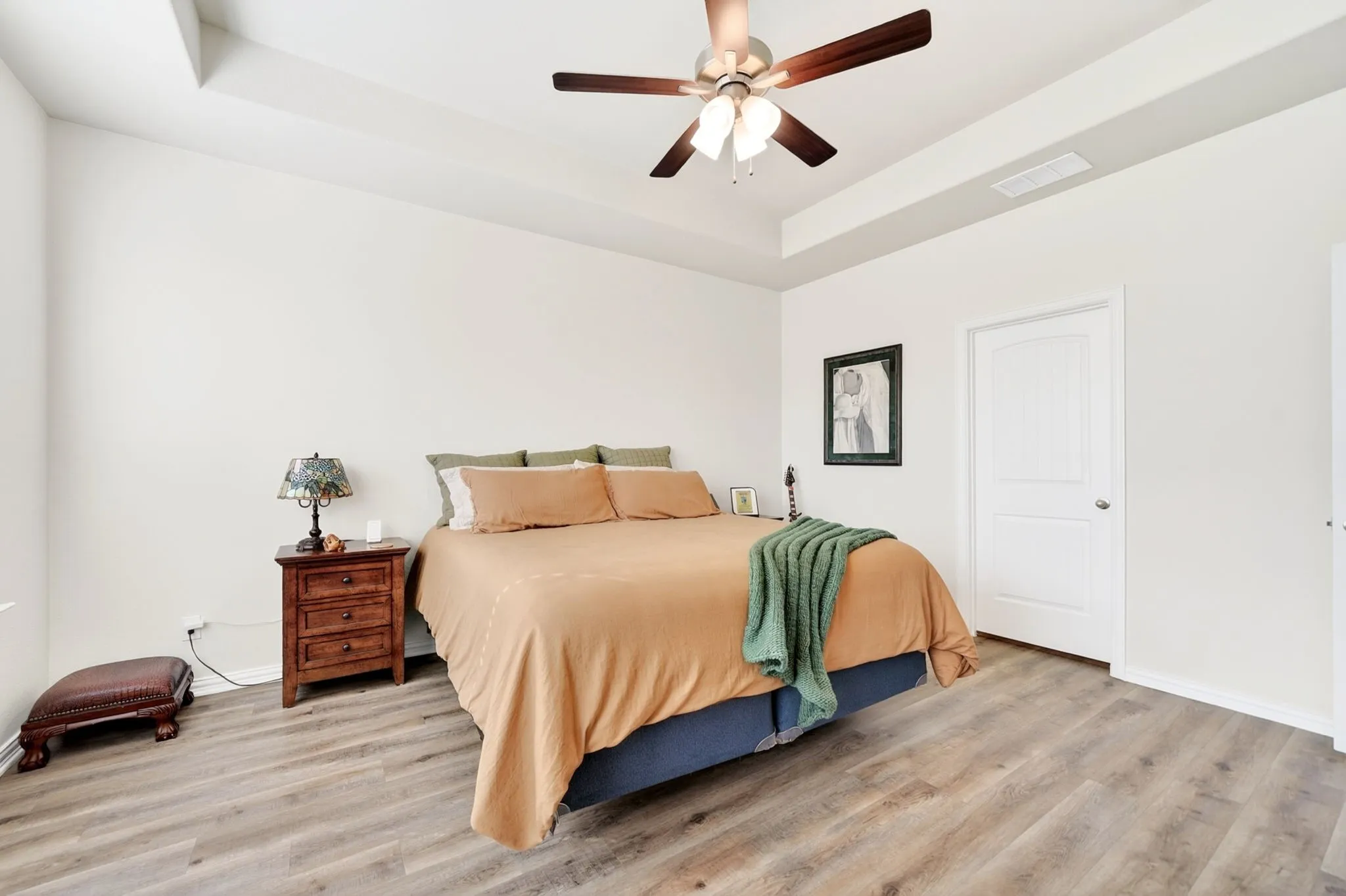 Spacious bedroom featuring wood-finish flooring, a tray ceiling, and a ceiling fan with integrated lighting