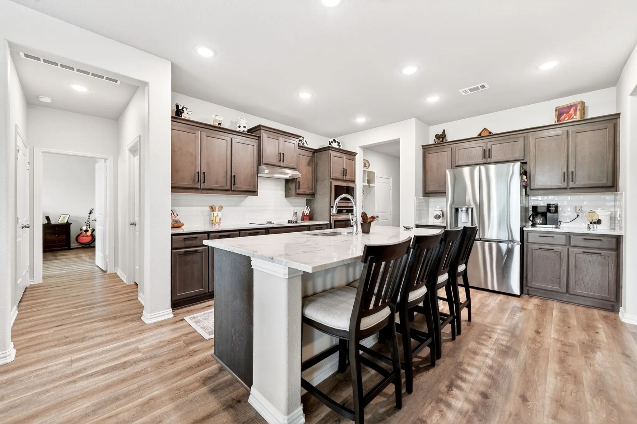 Kitchen featuring a central island with countertop seating, wood-finish flooring, stainless steel appliances, dark wood cabinetry, and recessed lighting