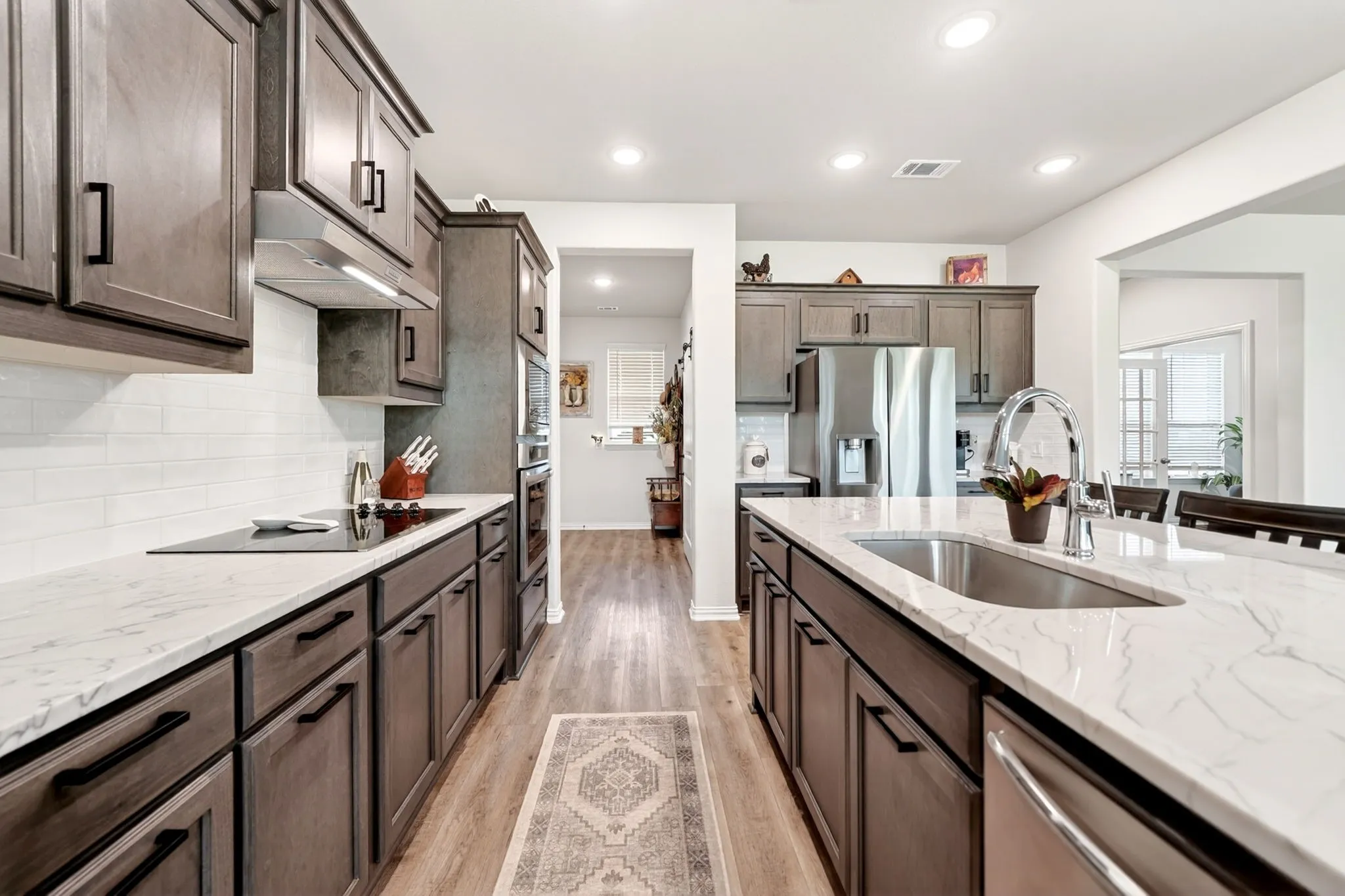 Modern kitchen featuring an expansive island with an undermount sink, white countertops with veining, wood-finish flooring, recessed lighting, and stainless steel appliances