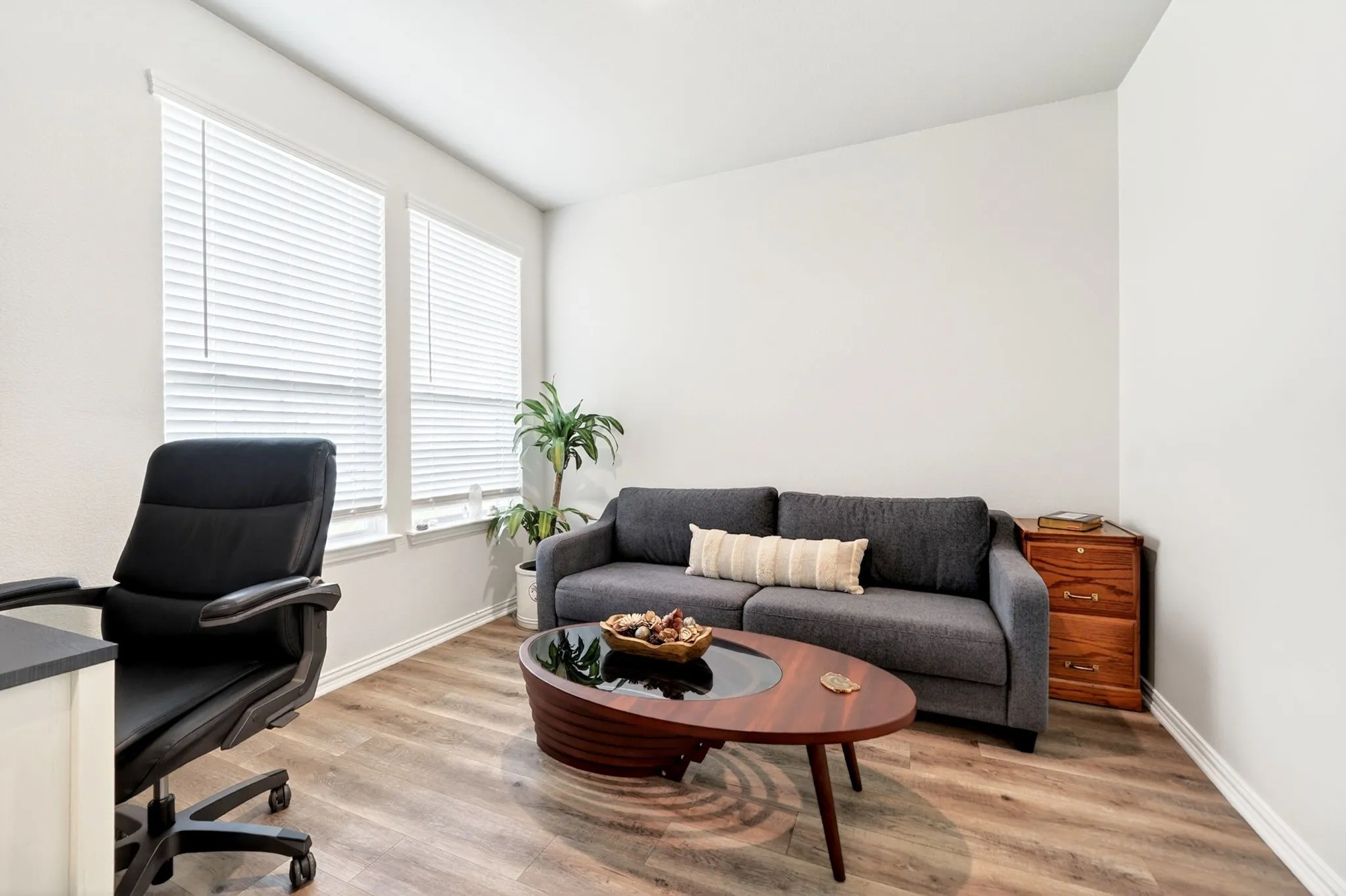 Room featuring wood-finish flooring, white baseboards, and two windows with blinds